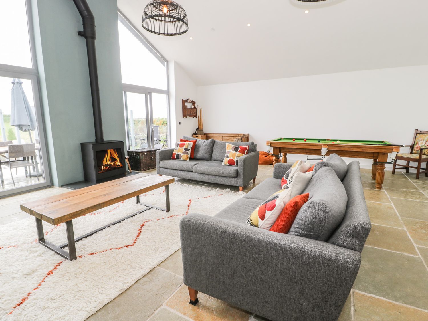 A living room with two gray sofas a wooden coffee table a rug a fireplace and a pool table at Cae Sam in Pentraeth