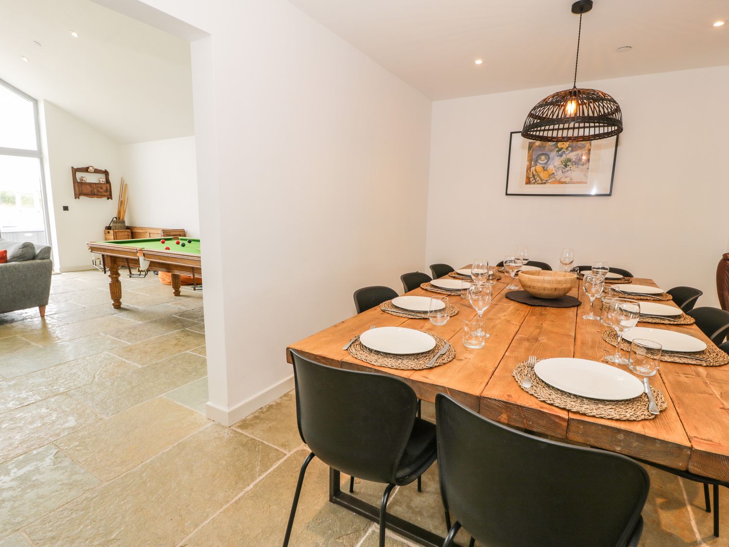 A dining room with a wooden table set with plates and glasses and a billiards room with a pool table at Cae Sam in Pentraeth