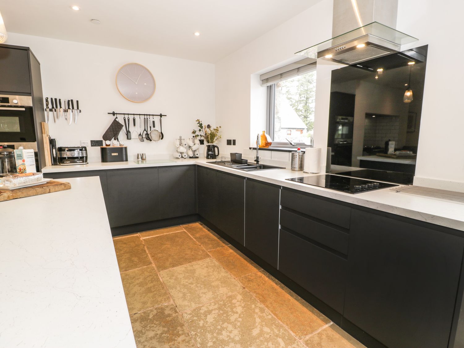 A kitchen with black cabinets white countertops a window and cooking utensils at Cae Sam in Pentraeth