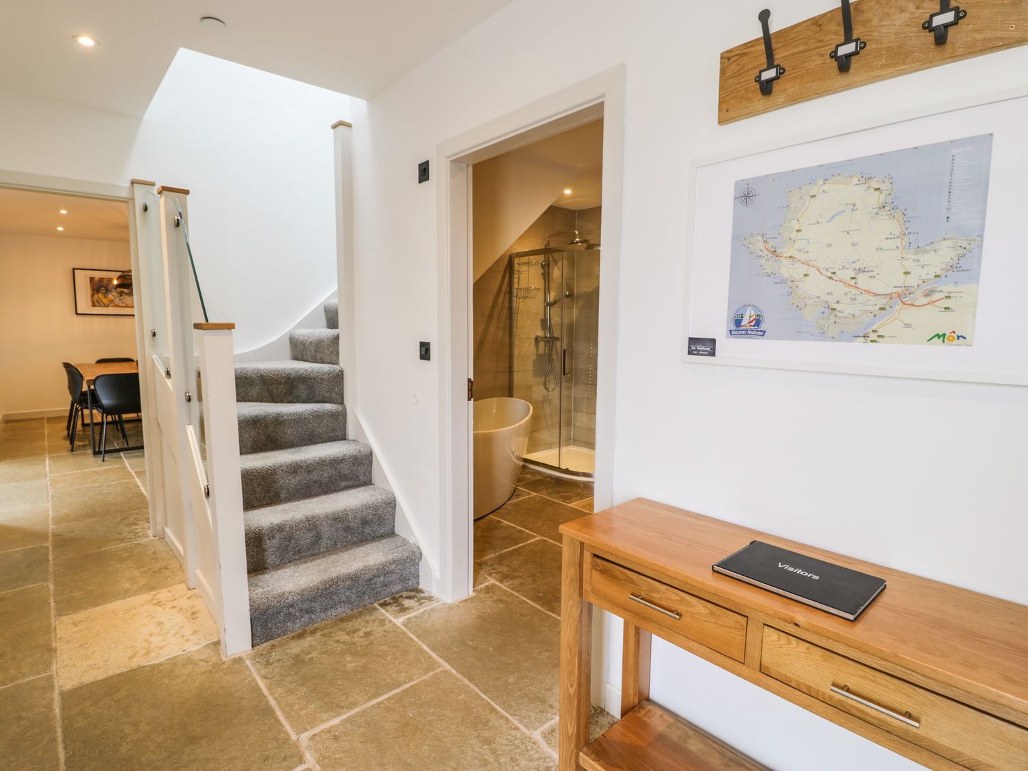 A hallway with carpeted stairs a wooden console table and a bathroom with a bathtub and shower visible at Cae Sam in Pentraeth