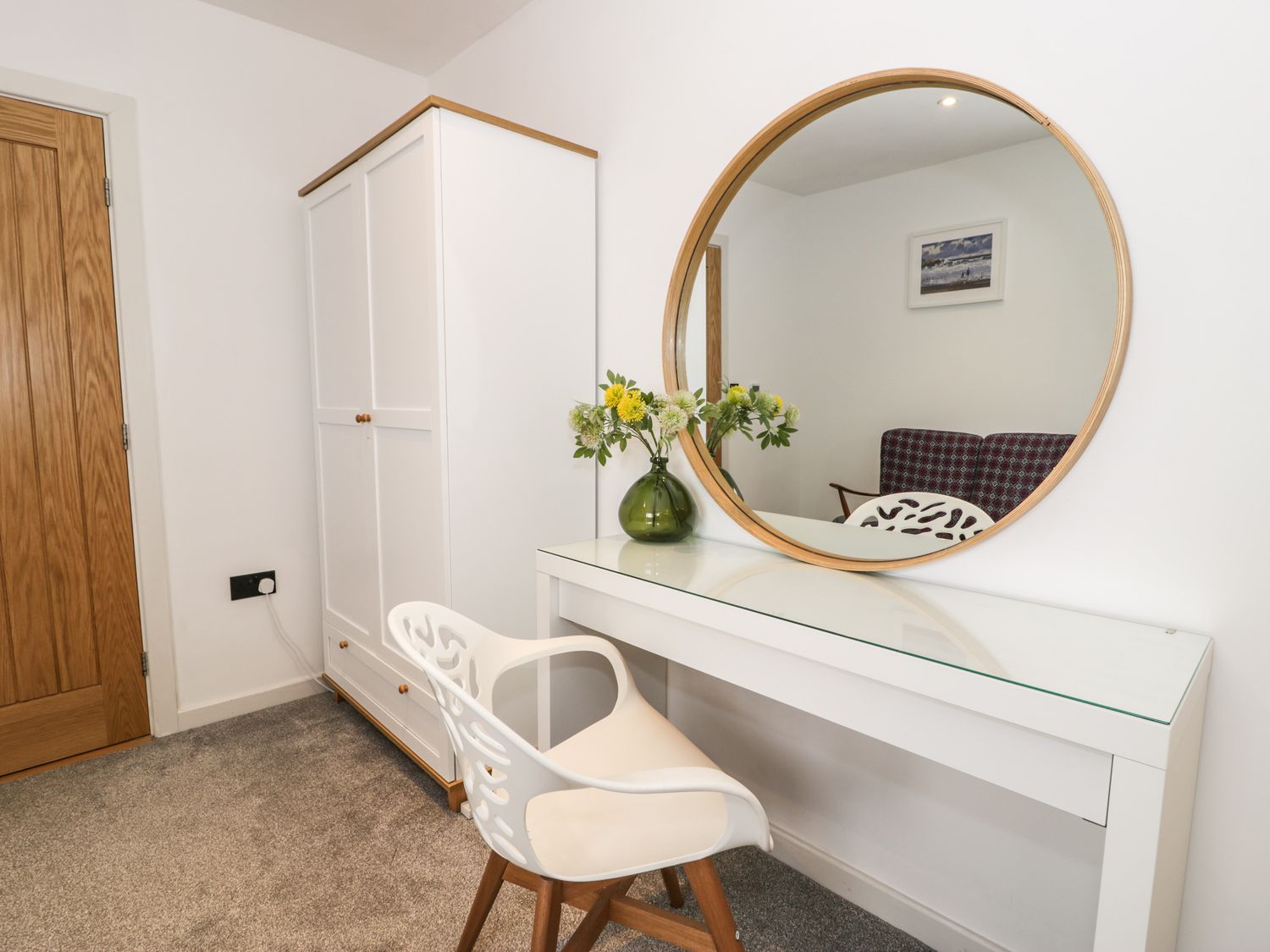 A room with a white wardrobe a white vanity table a round mirror and a white chair with wooden legs at Cae Sam in Pentraeth