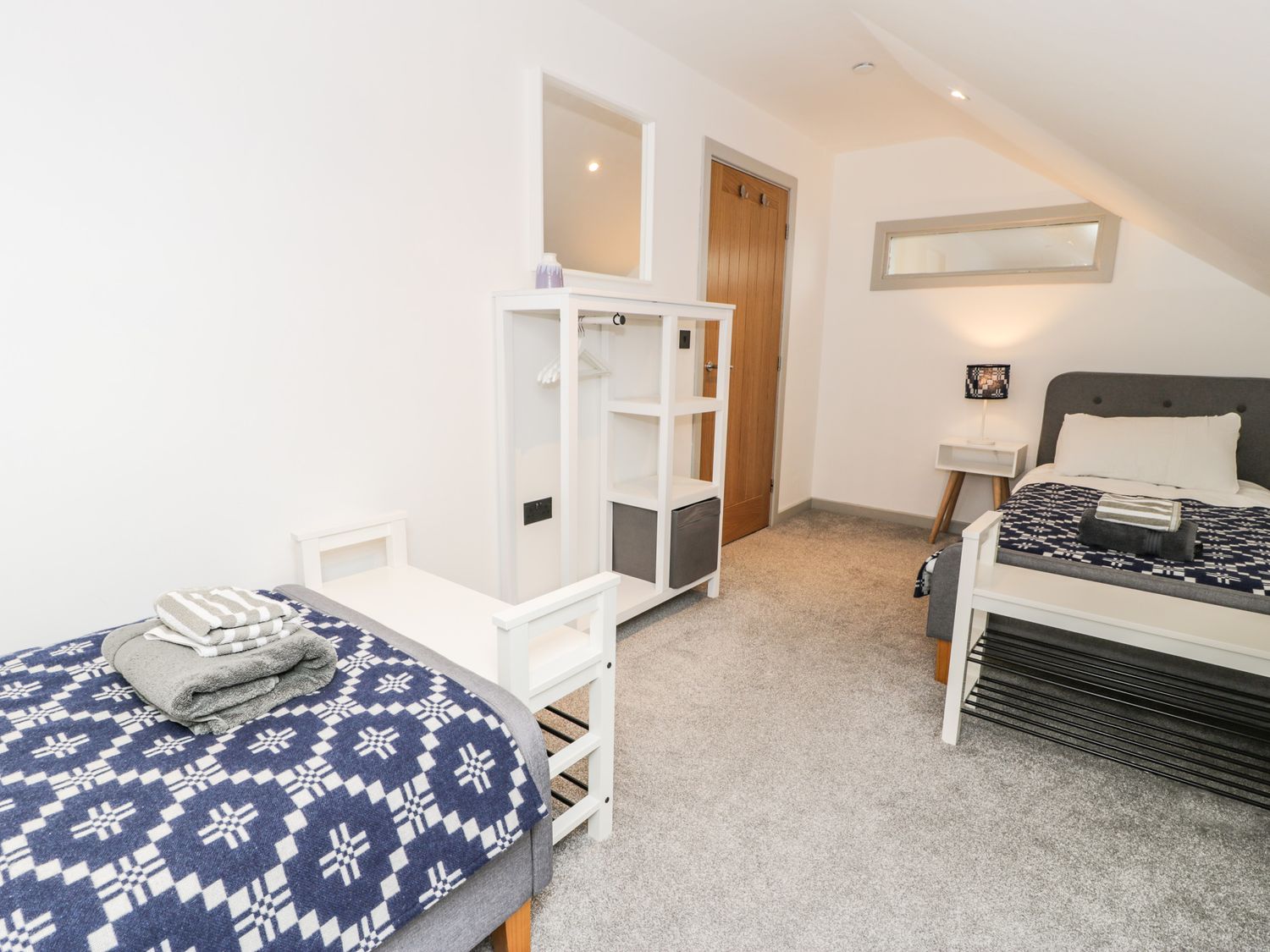 A bedroom with two single beds a white shelving unit with mirror and a wooden door at Cae Sam in Pentraeth