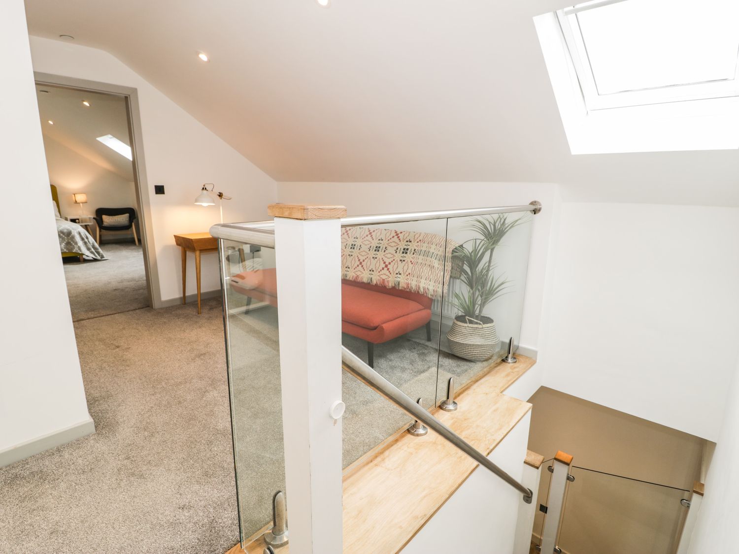 A landing area with a red chair a wooden side table and a plant next to a staircase at Cae Sam in Pentraeth
