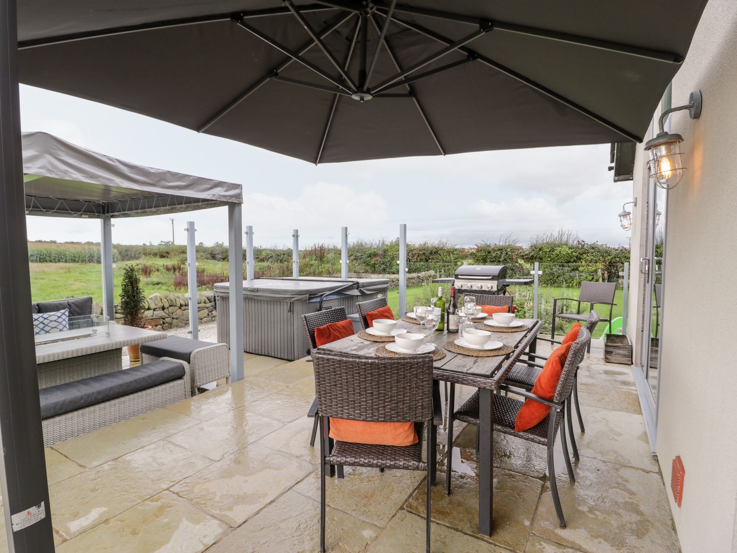 An outdoor patio with a dining table set with dishes and wine glasses under a large umbrella at Cae Sam in Pentraeth