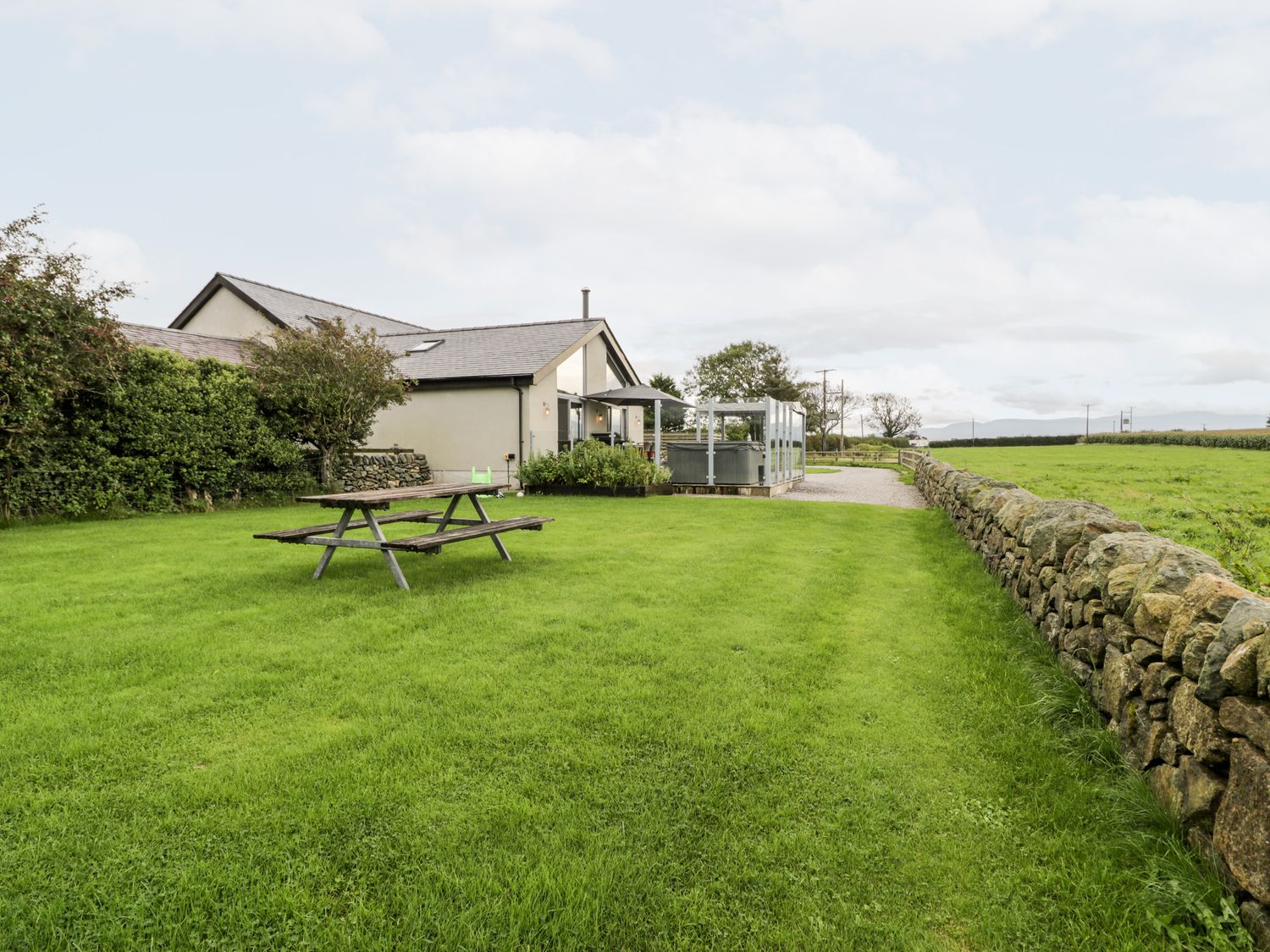 A backyard with a picnic table a hot tub and a grassy area next to a house at Cae Sam in Pentraeth
