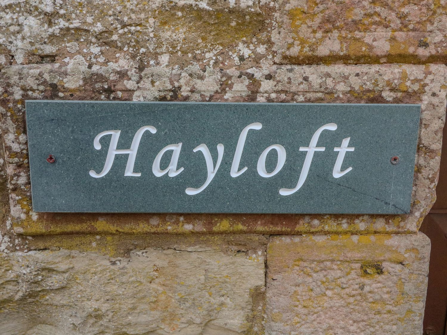 A stone wall with a green plaque showing the word Hayloft at Hayloft Cottage in Newbiggin-on-Lune