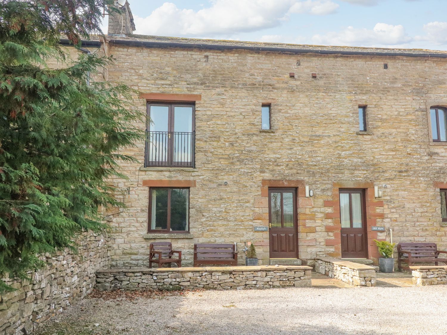 Stone cottage exterior with wooden doors and windows and benches outside at Hayloft Cottage in Newbiggin-on-Lune