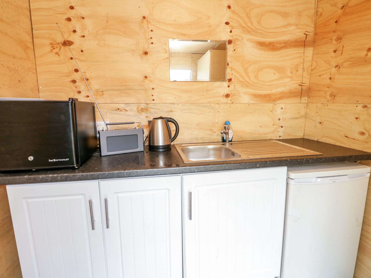 A kitchenette with a microwave, radio, electric kettle, sink, small refrigerator, and wooden walls at Heatherbank in Garelochhead