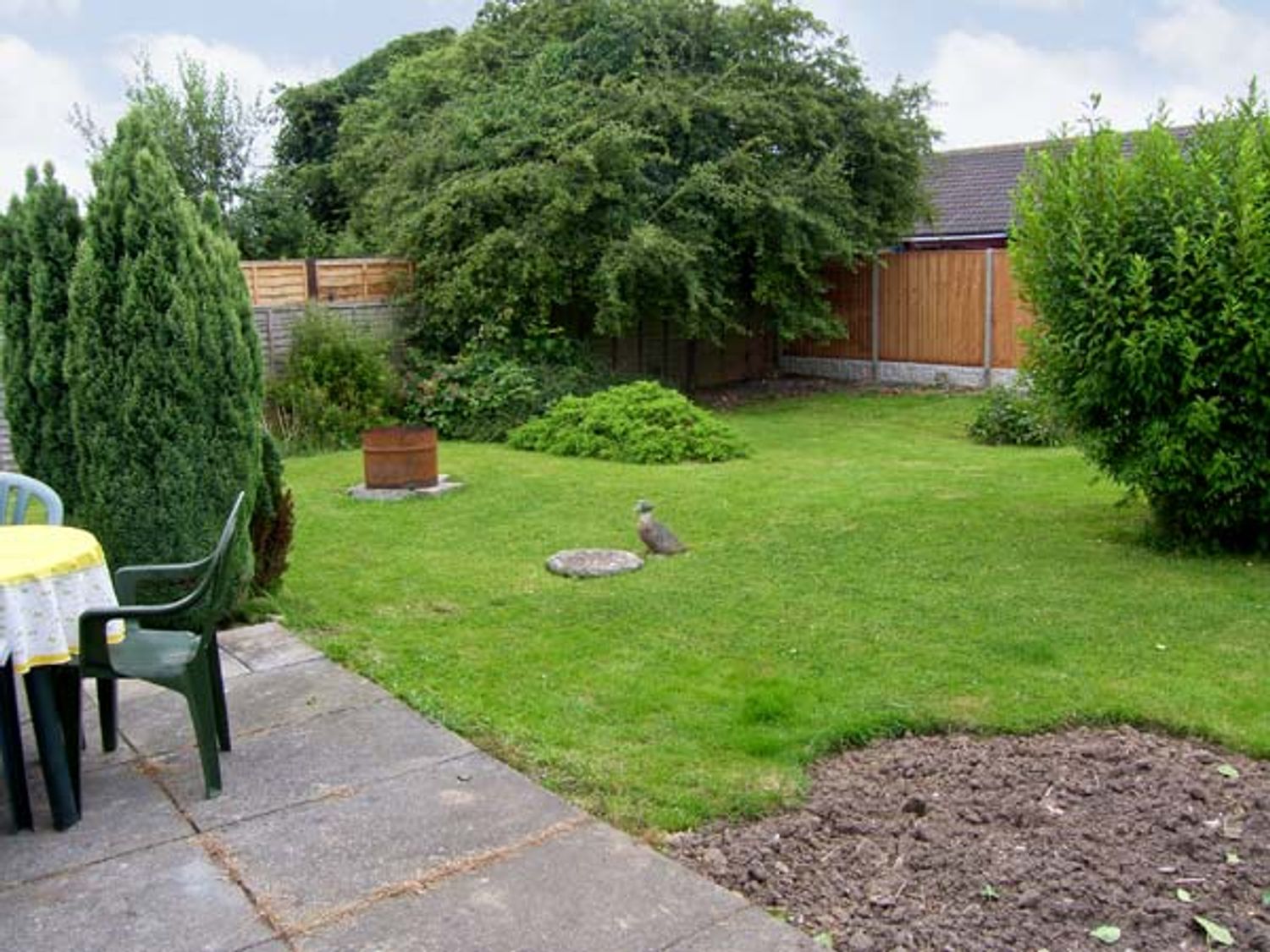 A backyard with a patio table and chairs a fire pit various bushes trees and grassy lawn at Sunnyside Cottage in Hogsthorpe near Skegness