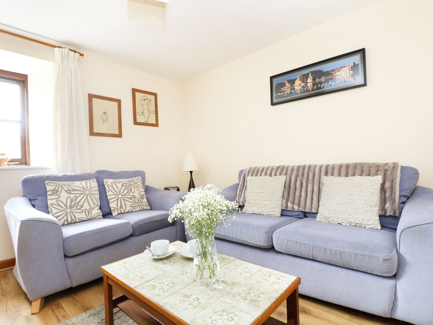 A living room with two blue sofas a coffee table with a vase of flowers and framed pictures on the wall at The Shippon Near Launceston