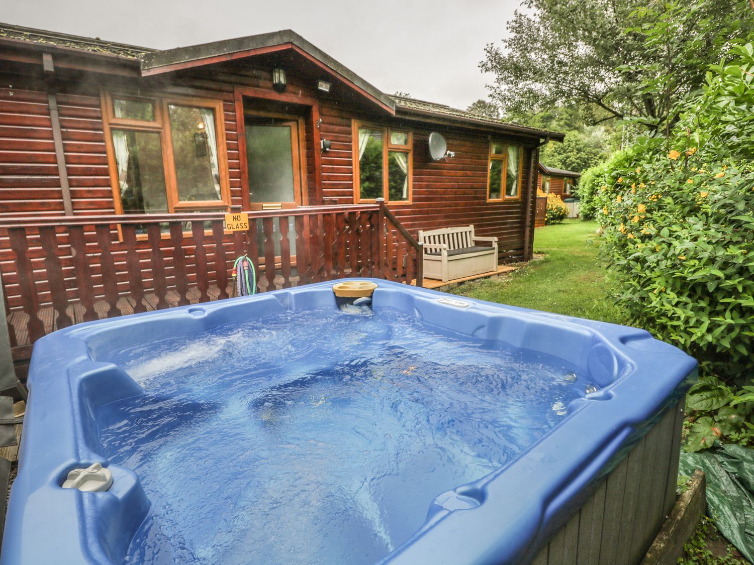 An outdoor hot tub with bubbling water next to a wooden cabin and green bushes at Langdale Lodge 15 White Cross Bay near Troutbeck Bridge