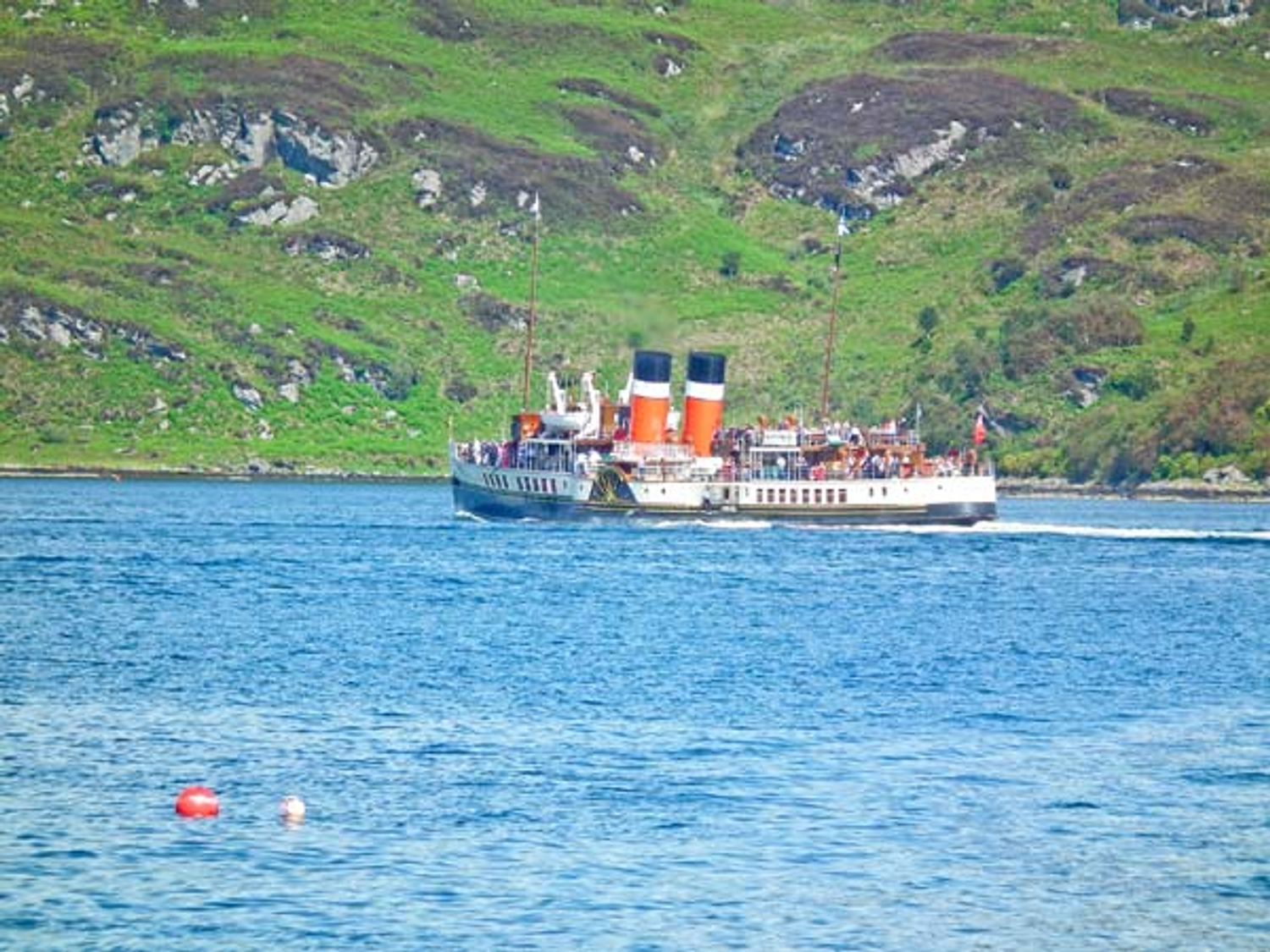 A passenger boat with two red and black chimneys on a body of water with green hills in the background at Top Flat in Tighnabruaich