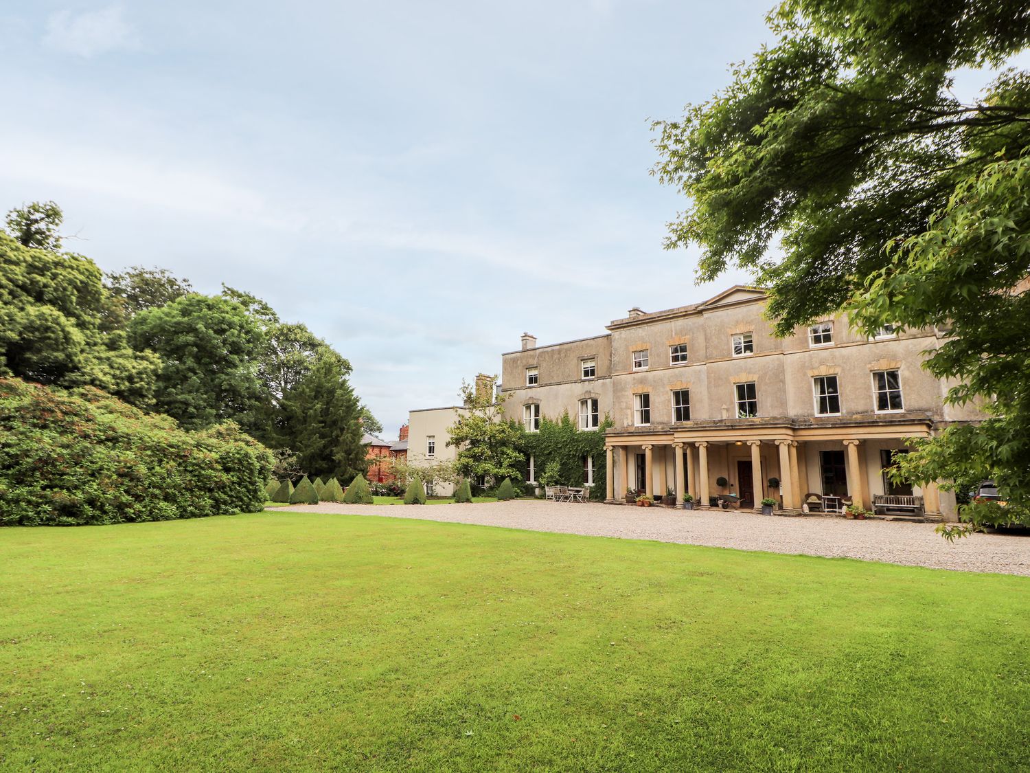A large historic building with columns and multiple windows surrounded by a lawn and trees at Cooks Flat in Cefn Park