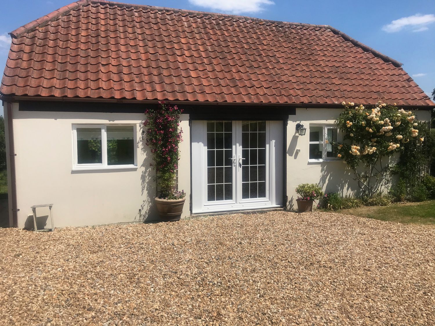 A single story building with a tiled roof two windows and a double glass door with plants and flowers outside at Oke Apple Cottage in Okeford Fitzpaine