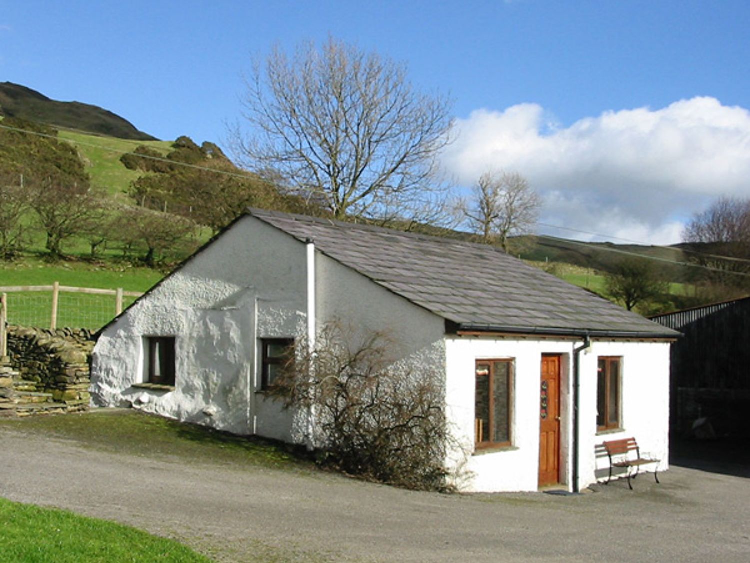 A small white cottage with a wooden door and windows with a bench outside in a rural setting at Ghyll Bank Bungalow Staveley near Windermere