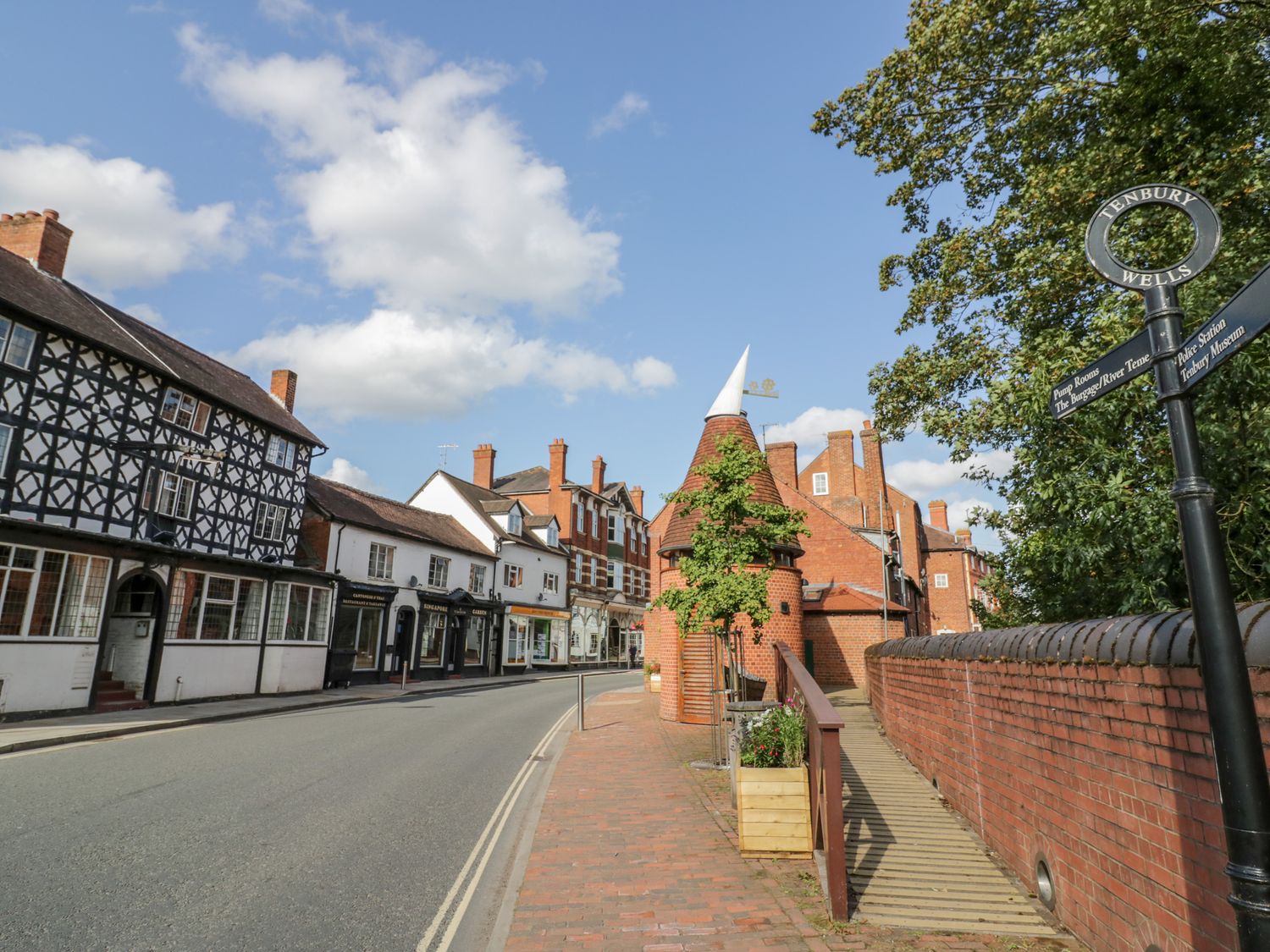 A street with historic buildings a brick sidewalk and a signpost reading Tenbury Wells