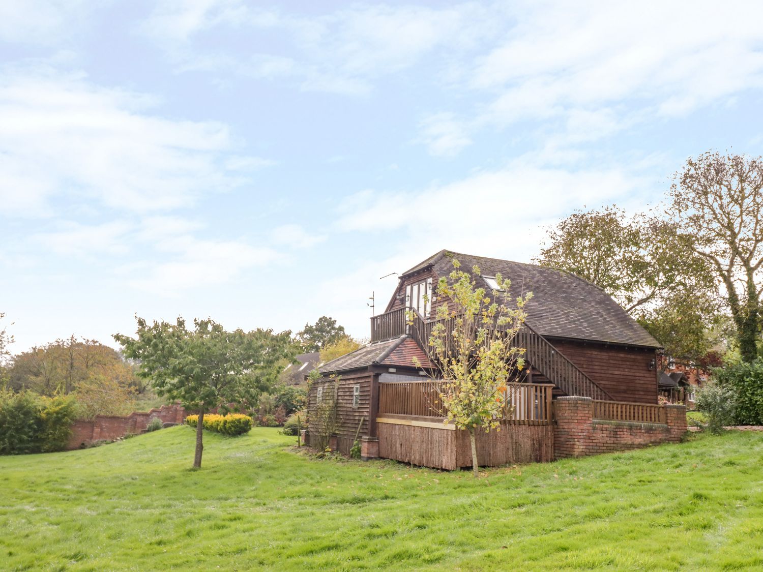 A wooden house with stairs and balcony surrounded by grass and trees at The Stilehouse Apartment in Menith Wood