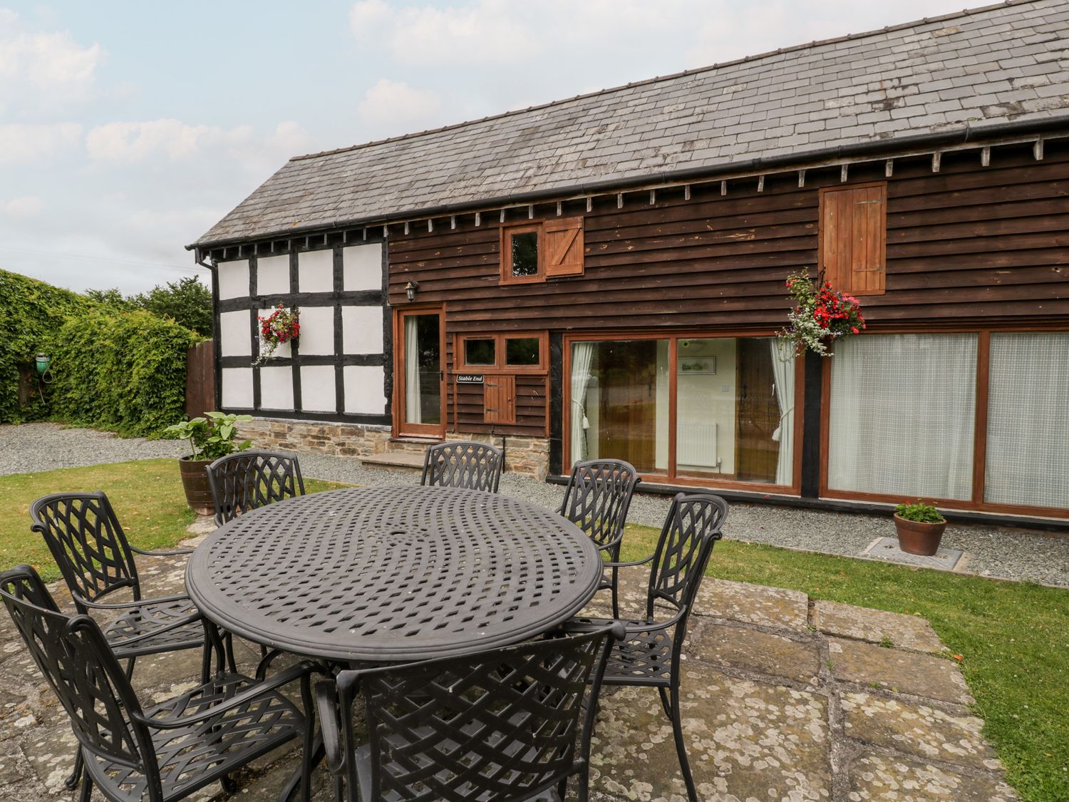 A round outdoor metal table with six chairs on a stone patio next to a timber and black and white painted building at Stable End in Luntley near Pembridge