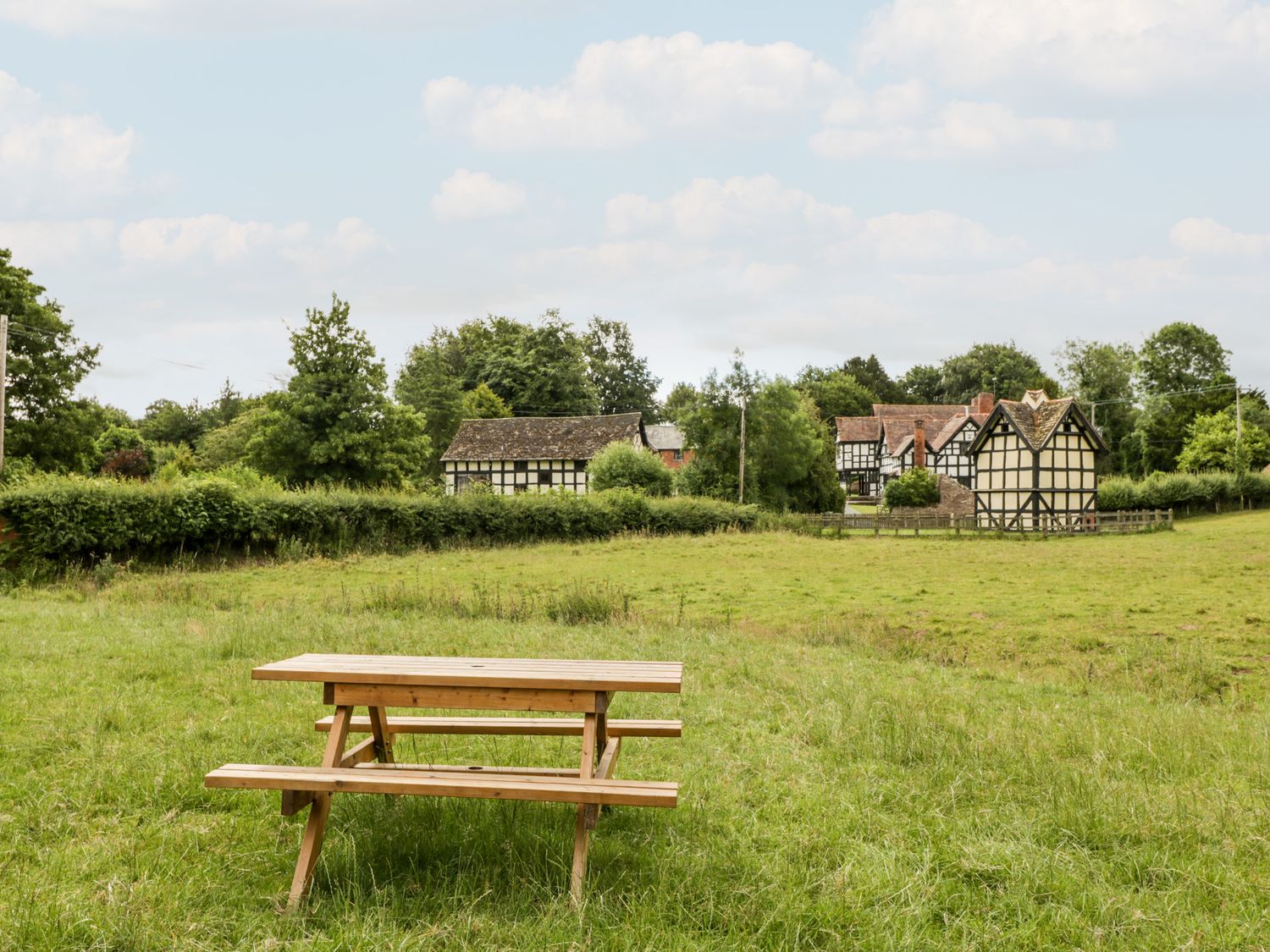 A wooden picnic bench on grass with traditional black and white buildings in the background at Stable End in Luntley near Pembridge