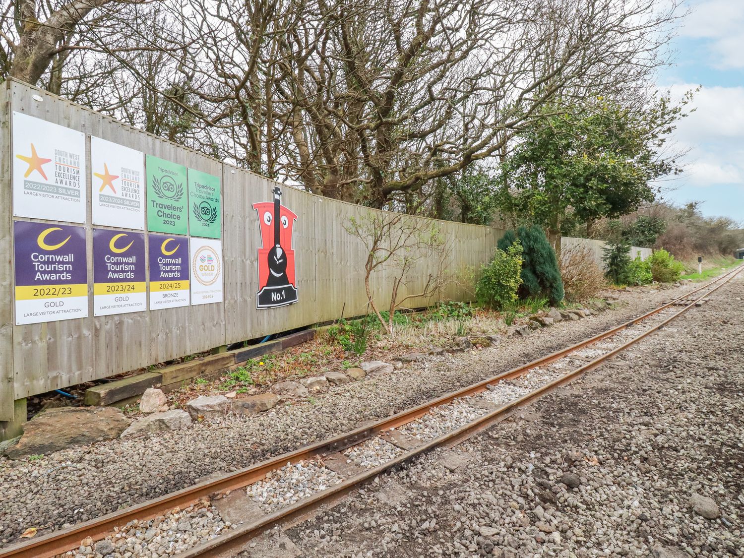 Railway tracks next to a wooden fence with award signs and trees behind it at The Station Flat in St Newlyn East near Newquay