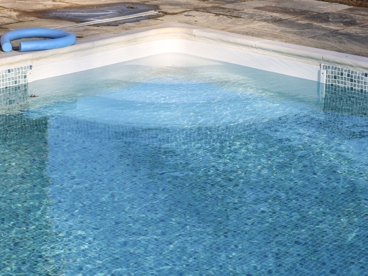 A clear blue swimming pool corner with tiled edges and a blue pool noodle on stone paving at Hoath House in Chiddingstone