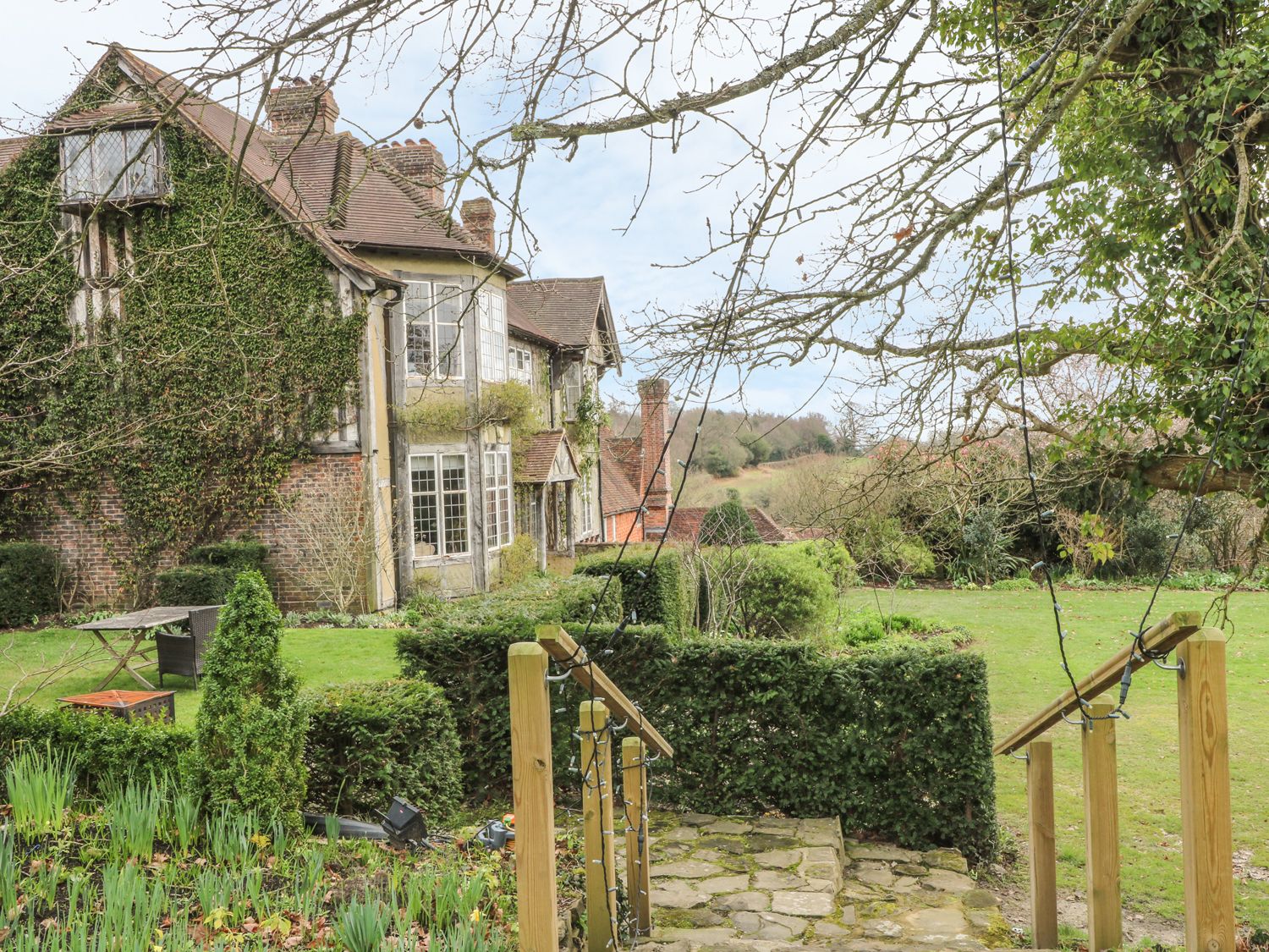 A garden with trimmed hedges and a stone path leading to a house covered in ivy at Hoath House in Chiddingstone