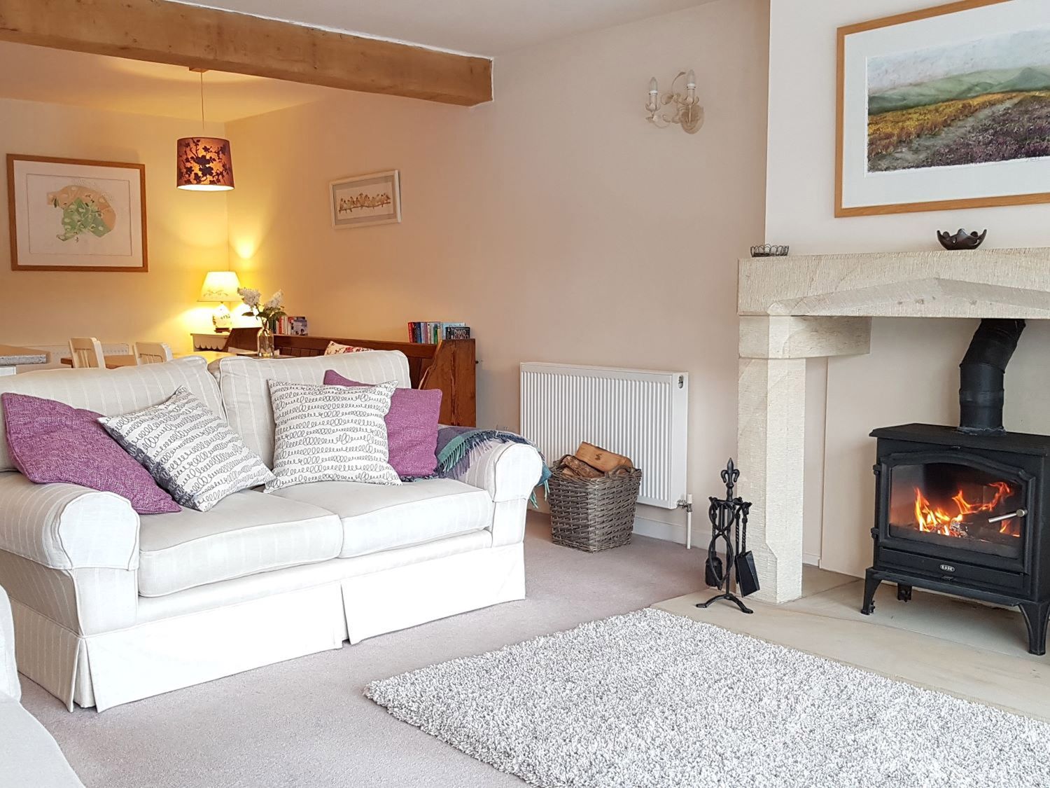 A living room with a couch and cushions next to a fireplace with fire at Stone Mouse Cottage in Bolton-By-Bowland