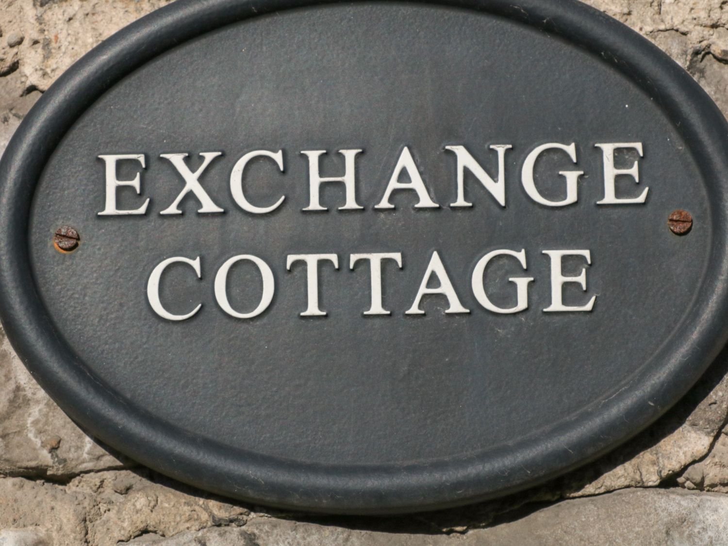 An oval black plaque with white text reading Exchange Cottage on a stone wall at Exchange Cottage in Tideswell