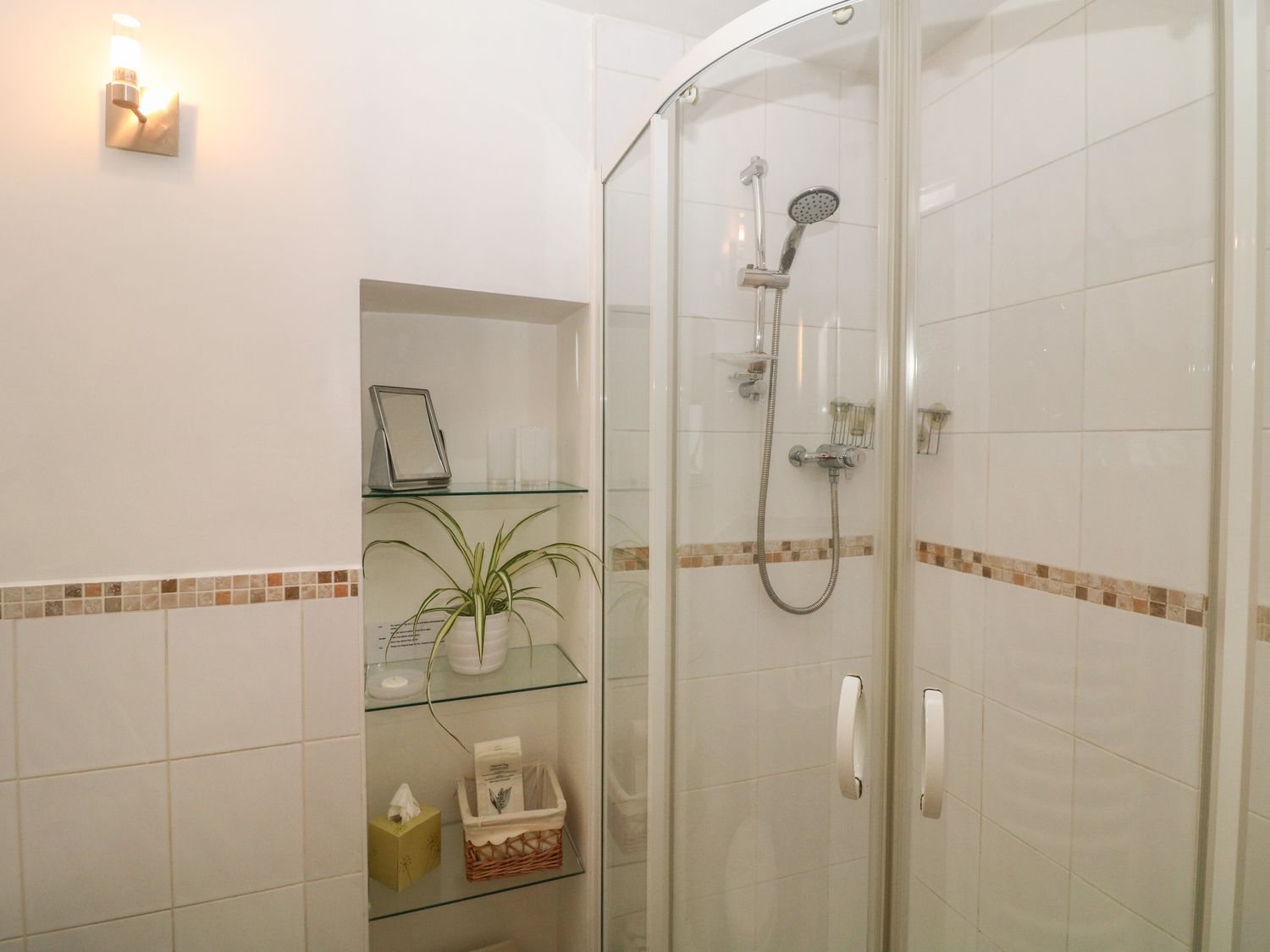 A tiled bathroom with a corner shower enclosure and built in glass shelves holding a plant and toiletries at Exchange Cottage in Tideswell