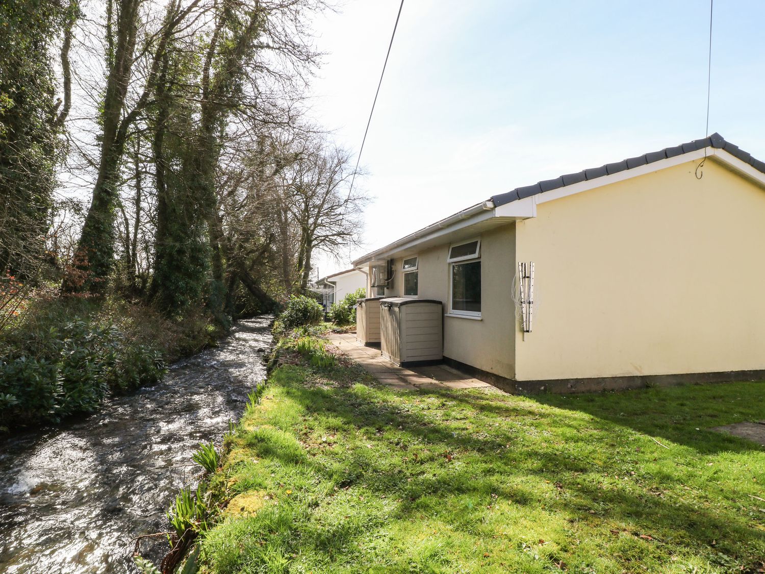 A yellow house next to a small flowing stream and grassy yard at 3 Rosecraddoc Lodge Rosecraddoc Lodge near Liskeard