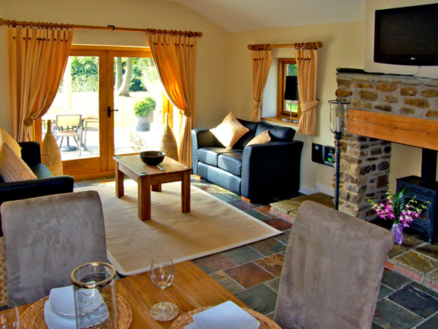 A living room with black sofas and beige cushions a wooden coffee table and a stone fireplace at Howle Hideaway in Howle Hill near Ross-on-Wye