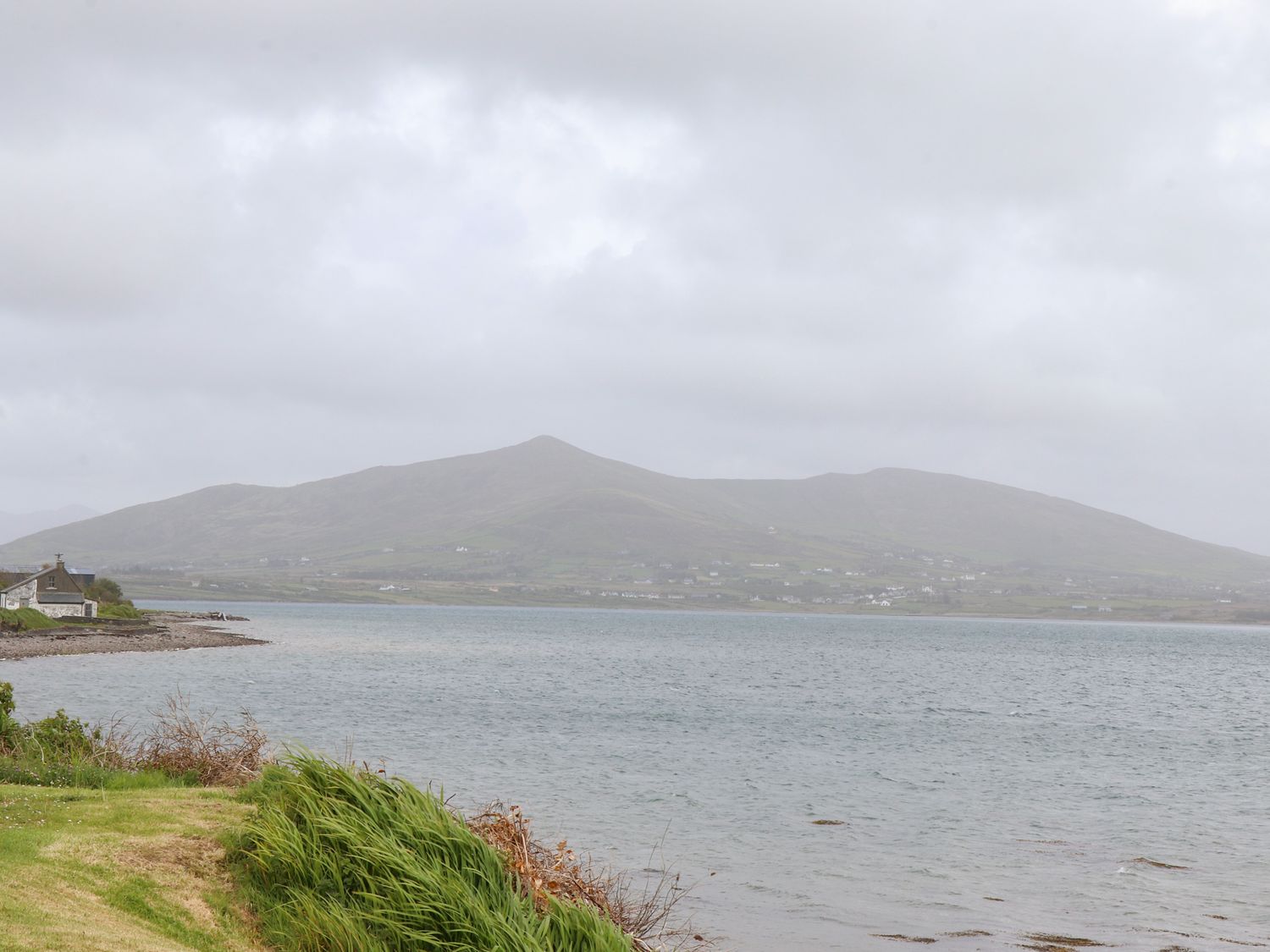 A coastline with grass in the foreground water in the middle and hills with scattered houses in the background at Brendans Cottage Valentia Island County Kerry
