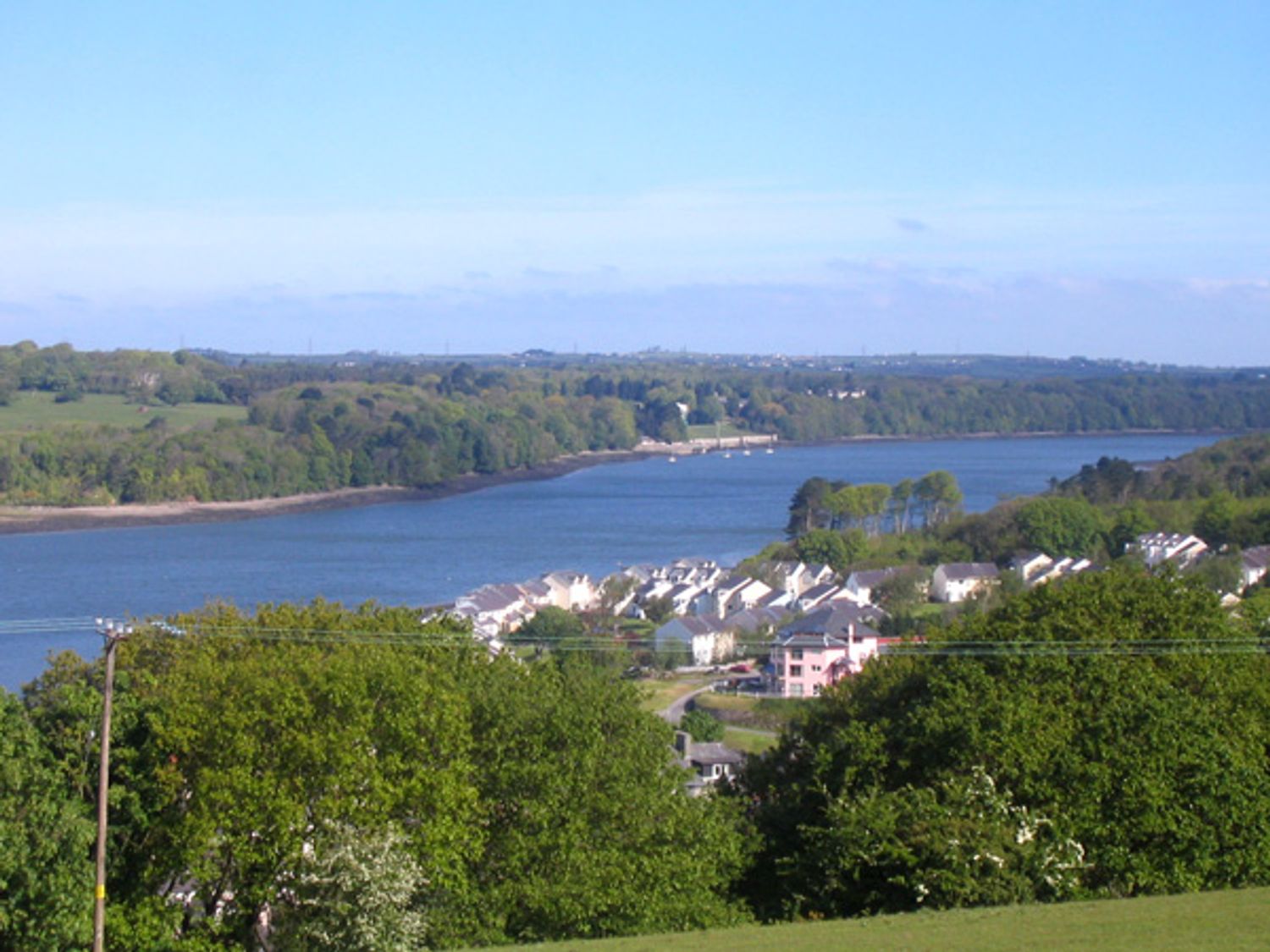 A river bordered by trees with houses on one side under a clear sky at Ysgubor Penrallt in Y Felinheli near Caernarfon