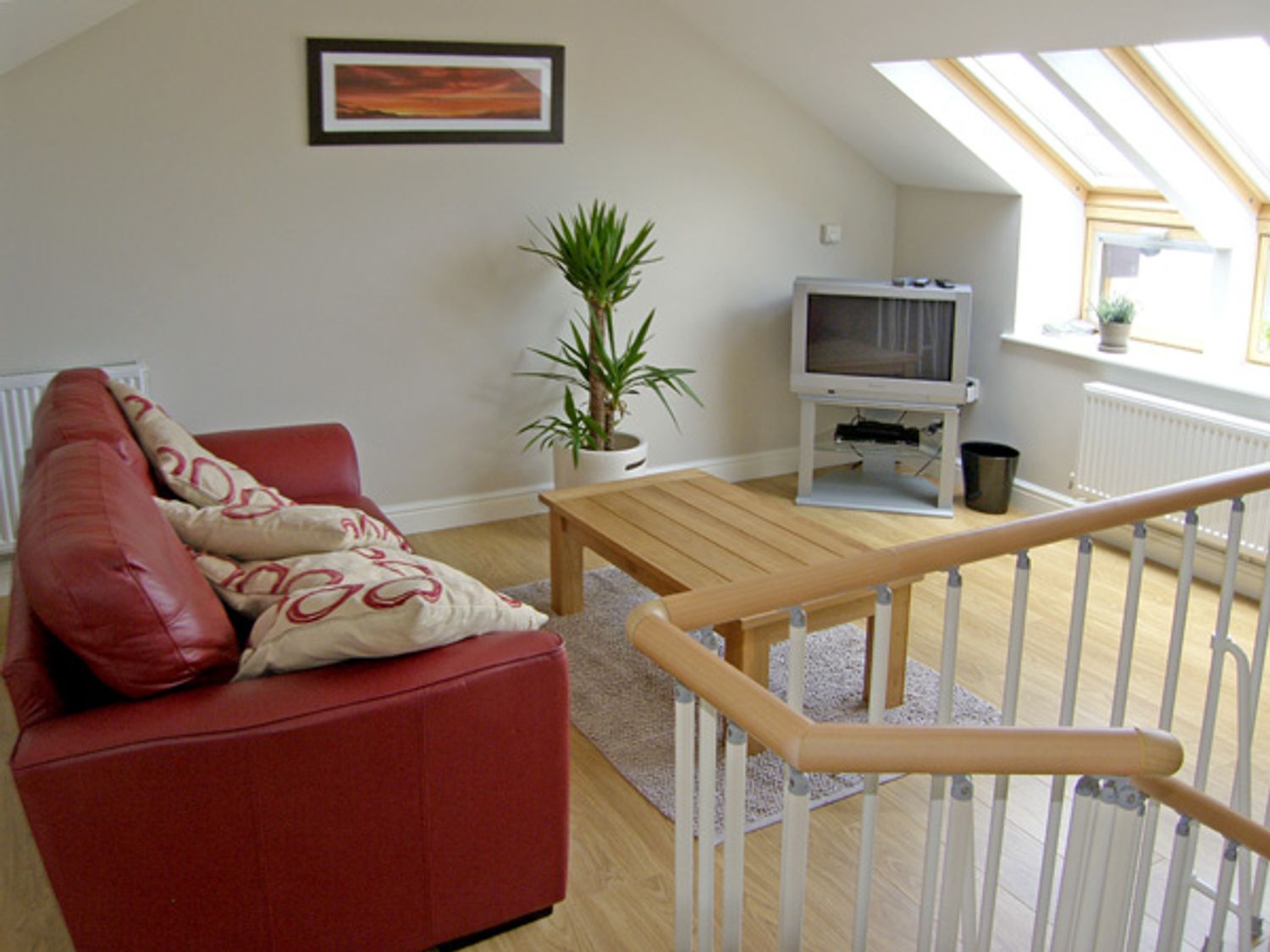 A living room with a red sofa wooden coffee table television plant and skylight windows at Ysgubor Penrallt in Y Felinheli near Caernarfon