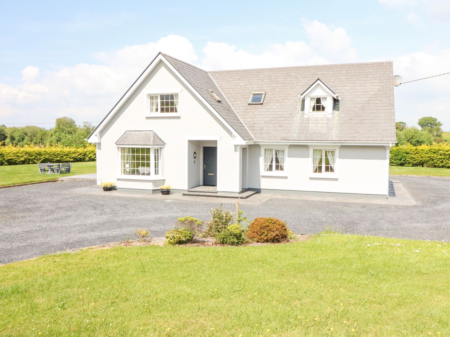 A white house with multiple windows and a grey roof surrounded by grass and a gravel driveway at Fern View House in Beaufort near Killorglin County Kerry