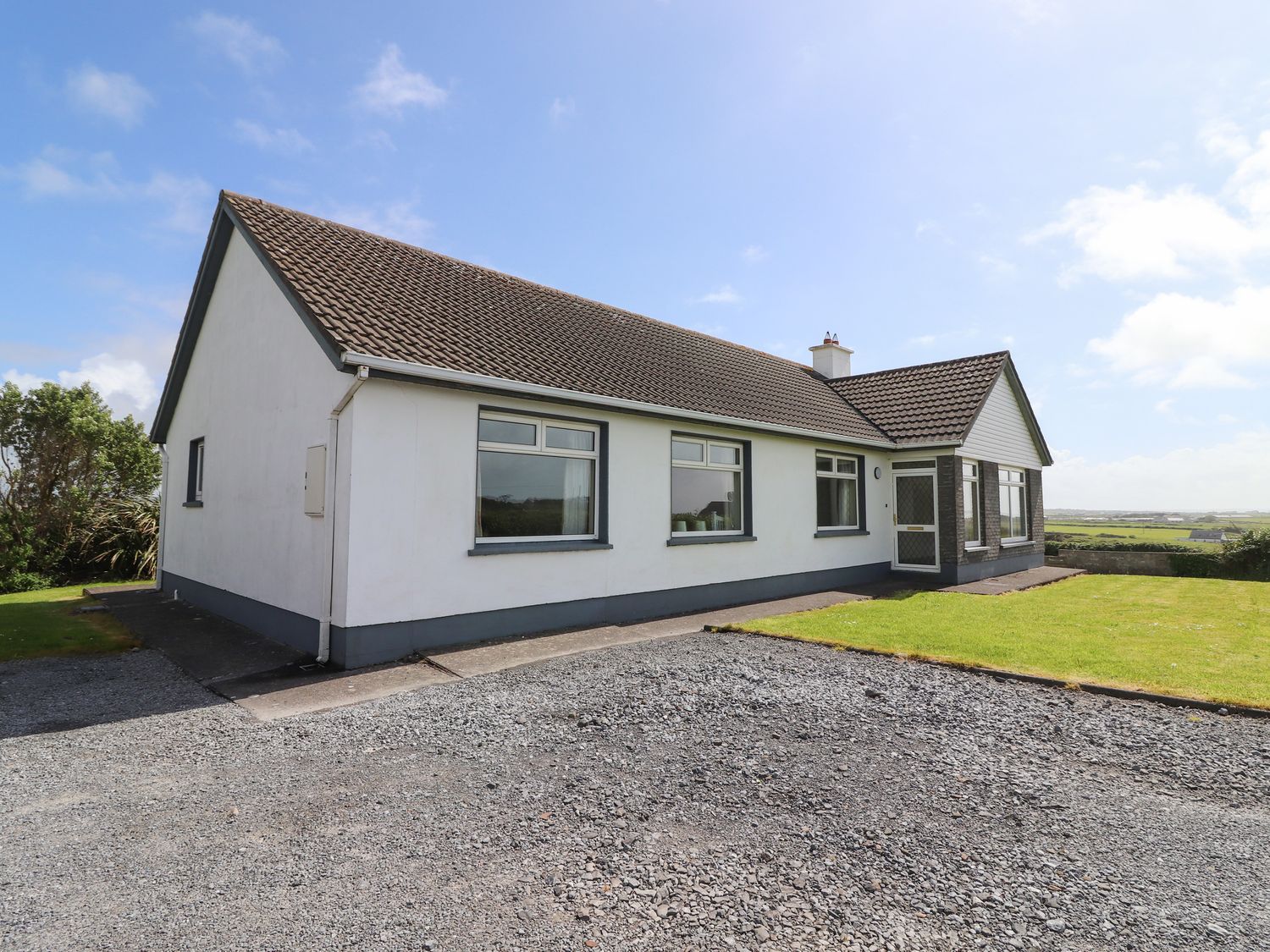 A single story house with a tiled roof gravel driveway and a lawn at Goodlands Cottage Spanish Point County Clare