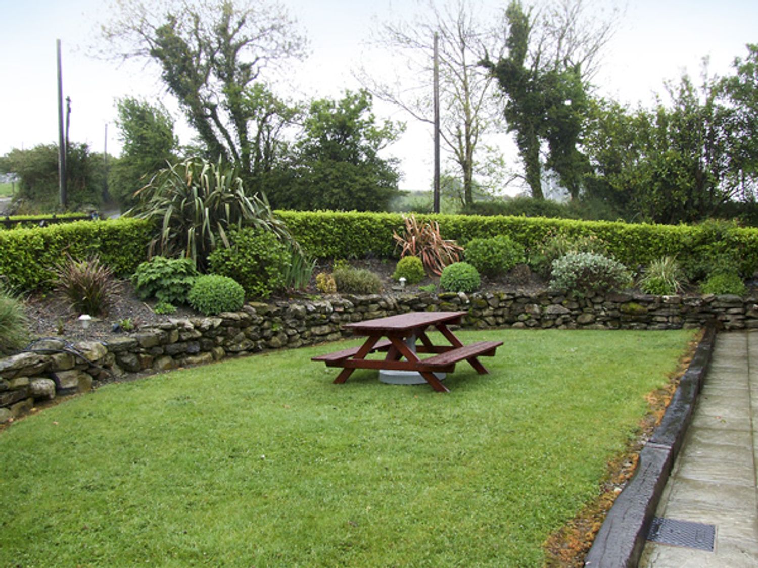 A garden with a wooden picnic table and stone wall surrounded by shrubs and trees at An Grianan in Clonakilty County Cork