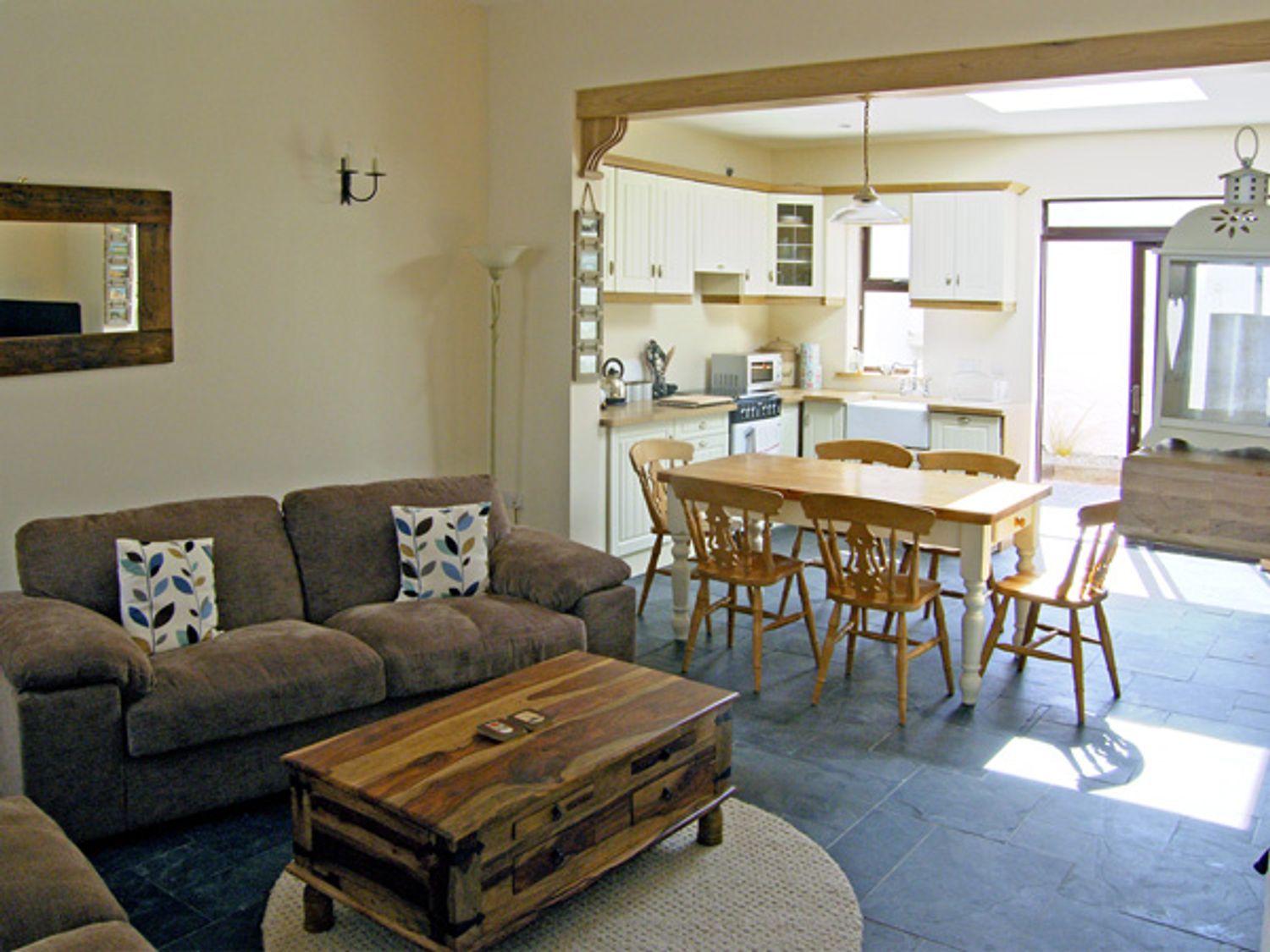 A living room with brown sofas and a wooden coffee table next to a kitchen with a dining table and chairs at Kilkee Cottage in Kilkee County Clare