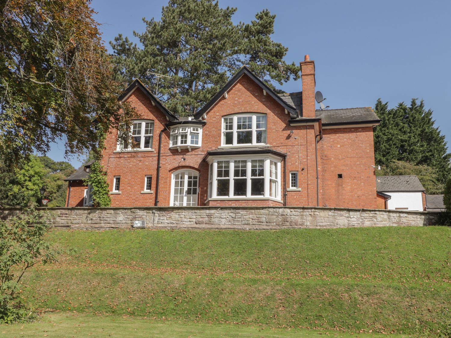 A red brick house with white framed windows and a stone wall in front surrounded by trees at The Croft in Vowchurch near Peterchurch