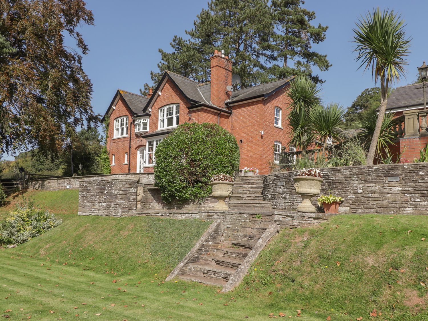 A red brick house with stone steps and a garden with trees and shrubs at The Croft in Vowchurch near Peterchurch