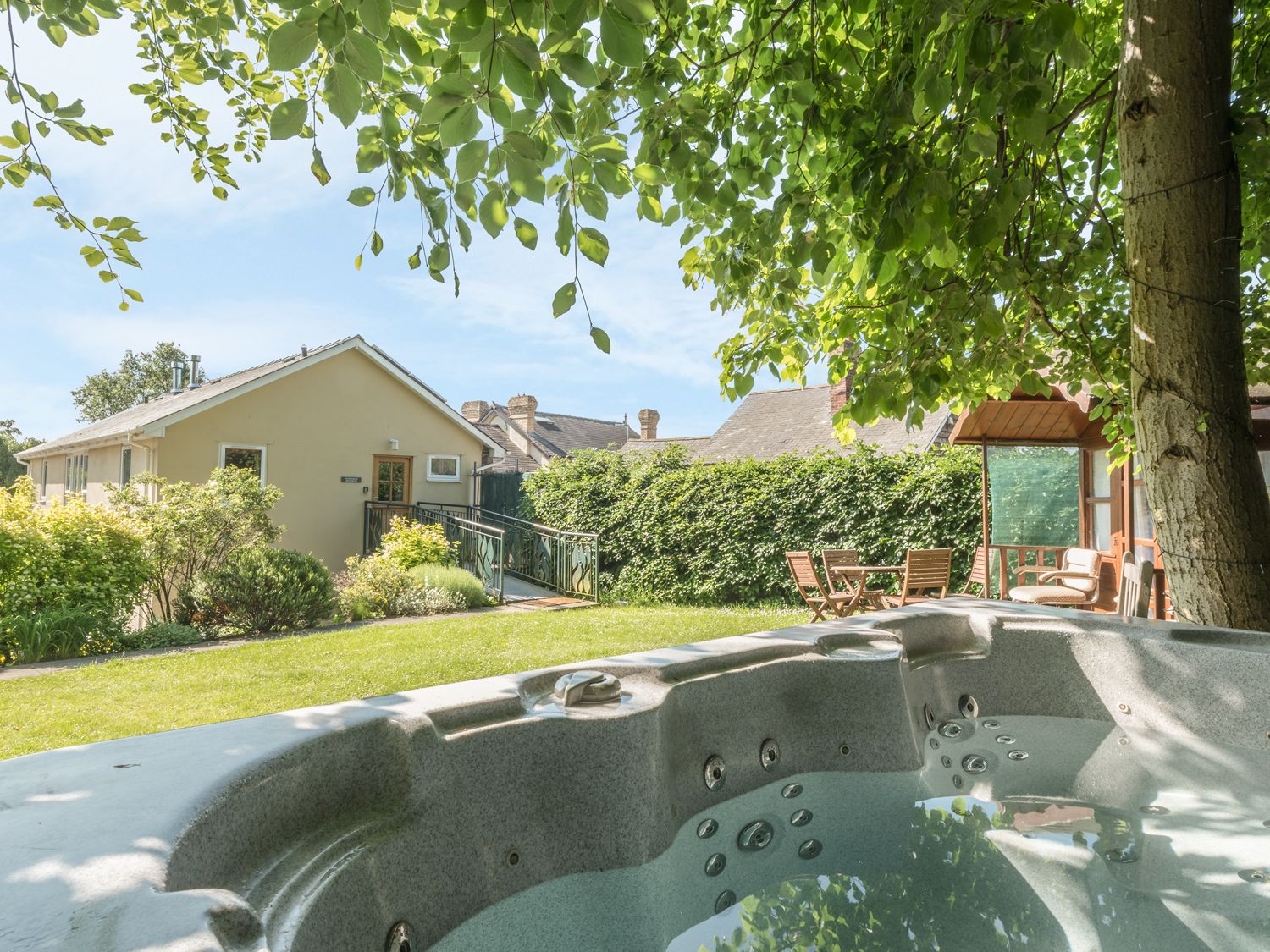 A garden with a hot tub under a tree and outdoor furniture near a building at The Schoolhouse Brewhouse in Bishops Castle