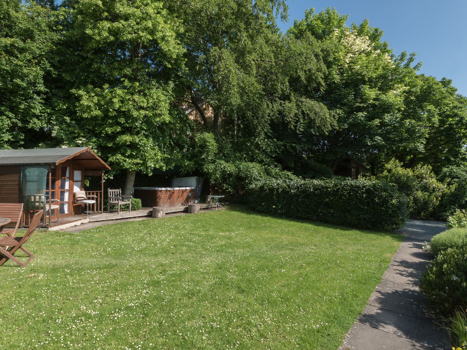 A garden with lawn chairs wooden shed and hot tub surrounded by trees and shrubs at The Schoolhouse Brewhouse in Bishop's Castle