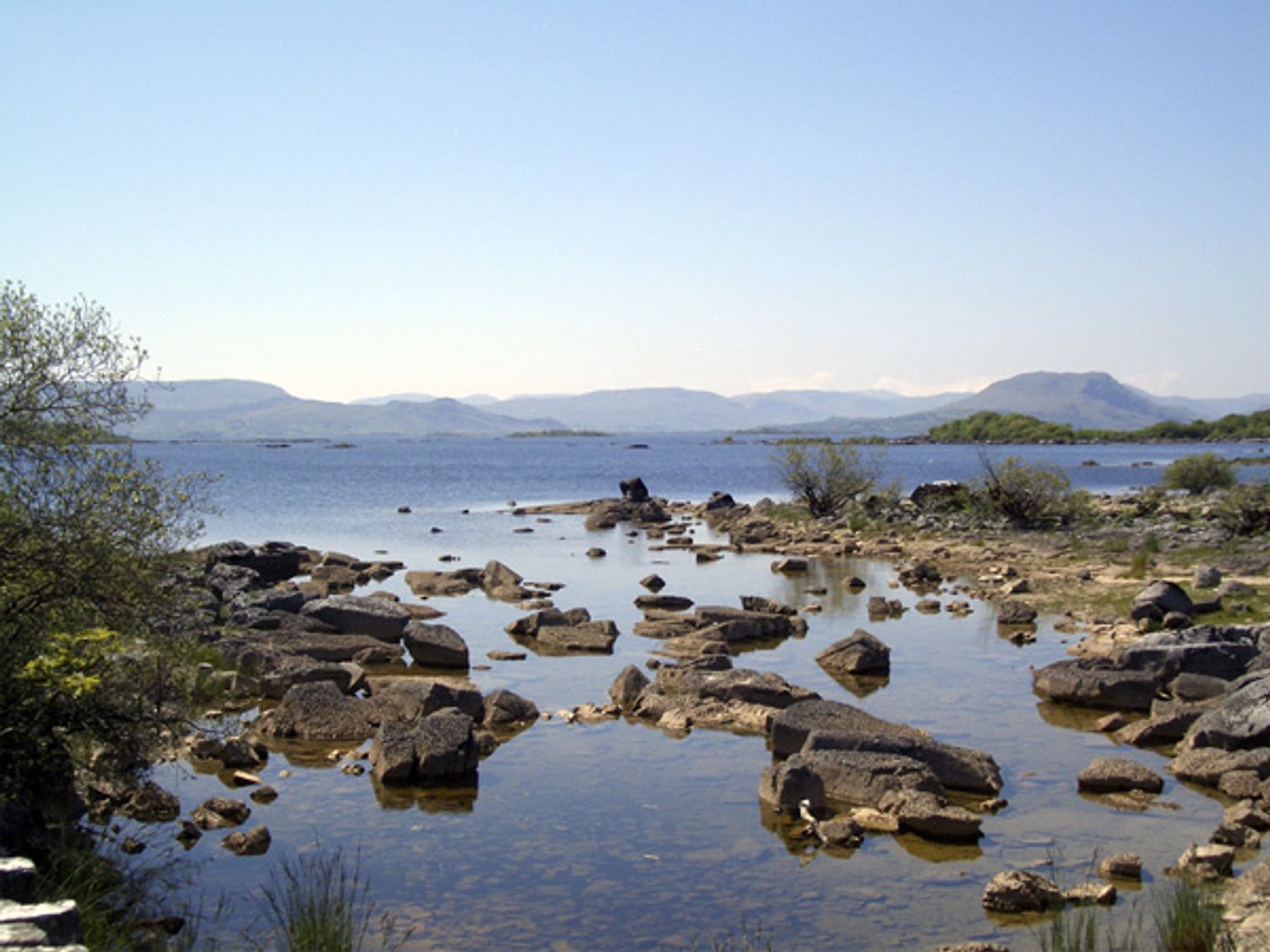 A rocky shoreline with water and hills in the background at Clooncorraun Cottage in Ballinrobe County Mayo