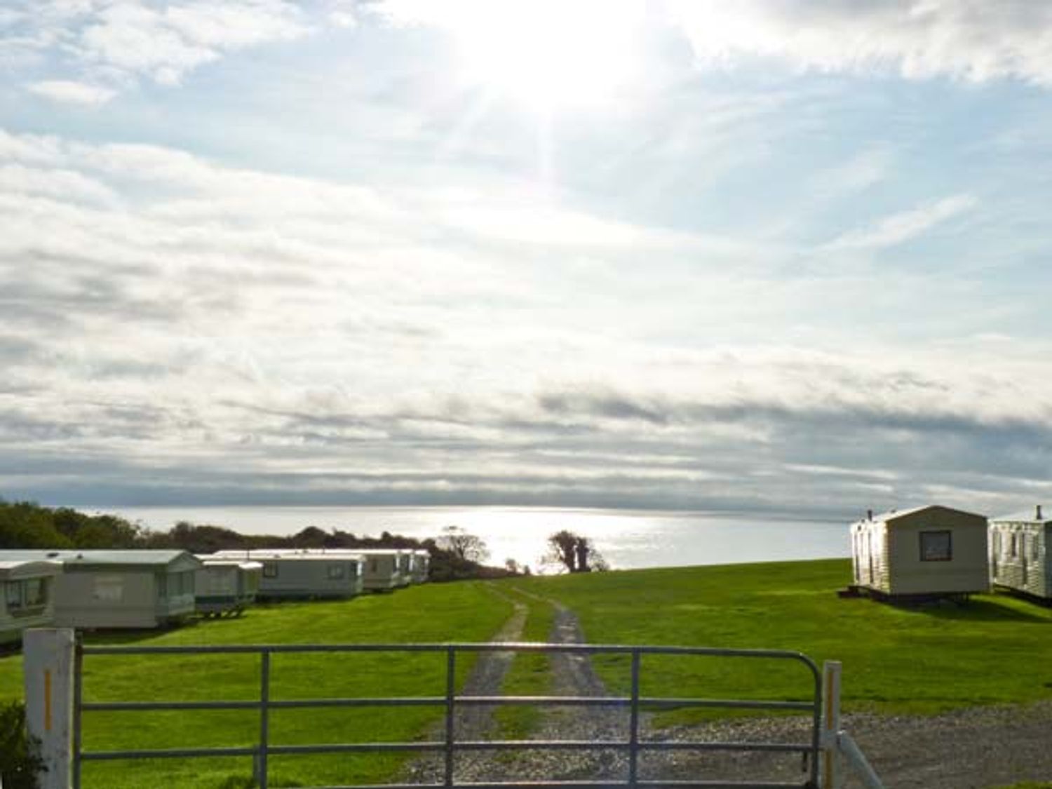 A grassy field with a gravel path and caravans near a body of water at Silver Strand Cottage Silver Strand near Wicklow Town County Wicklow