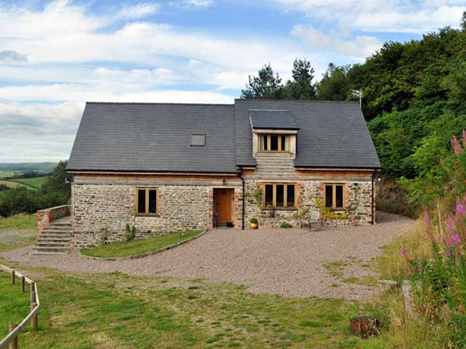 A stone house with a slate roof and wooden windows surrounded by grass and trees at Hiraeth in Dolau near Llandrindod Wells