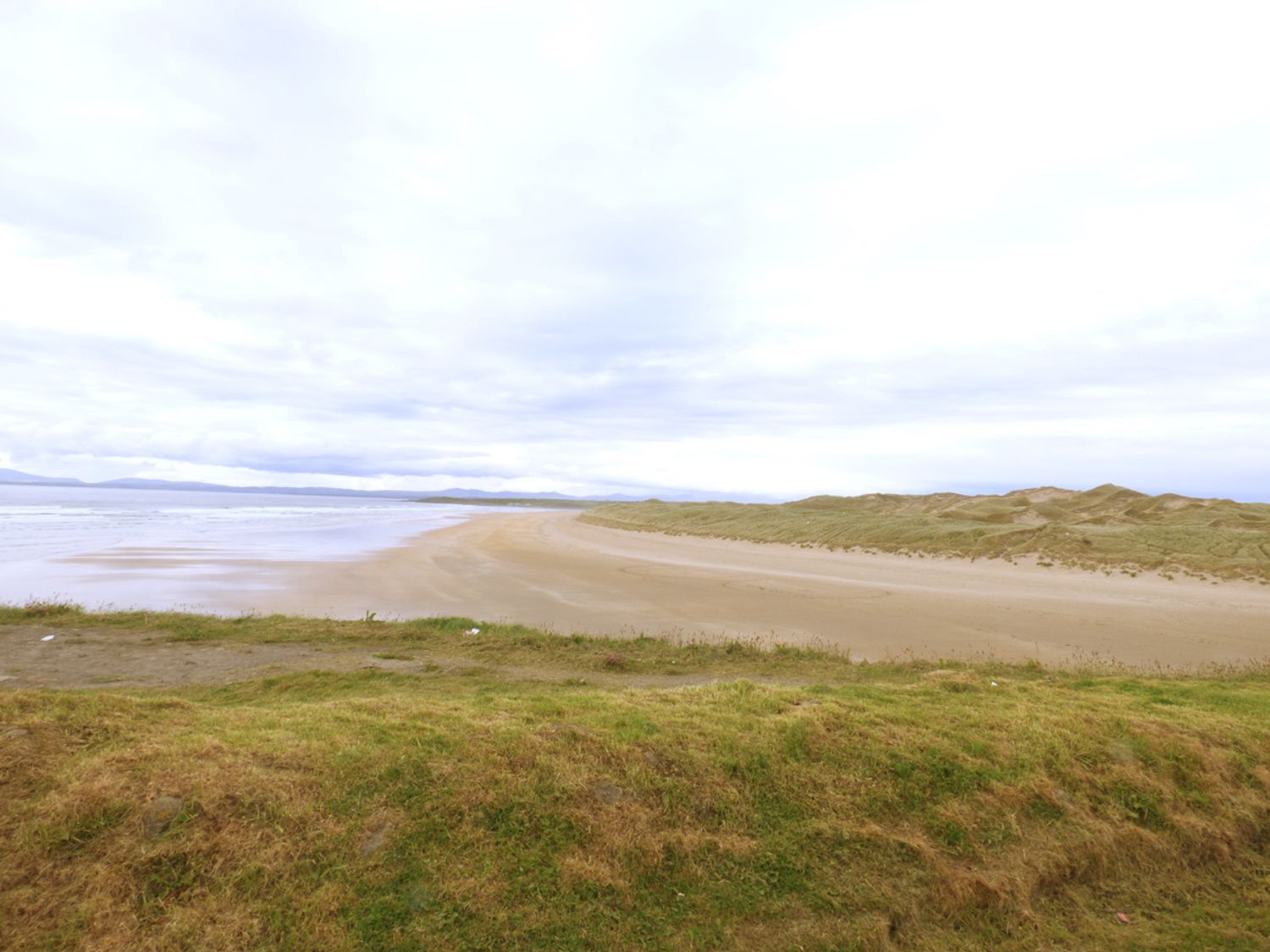 A sandy beach with grassy dunes and water under a cloudy sky at No 17 Mountain Dale in Tullaghan County Leitrim
