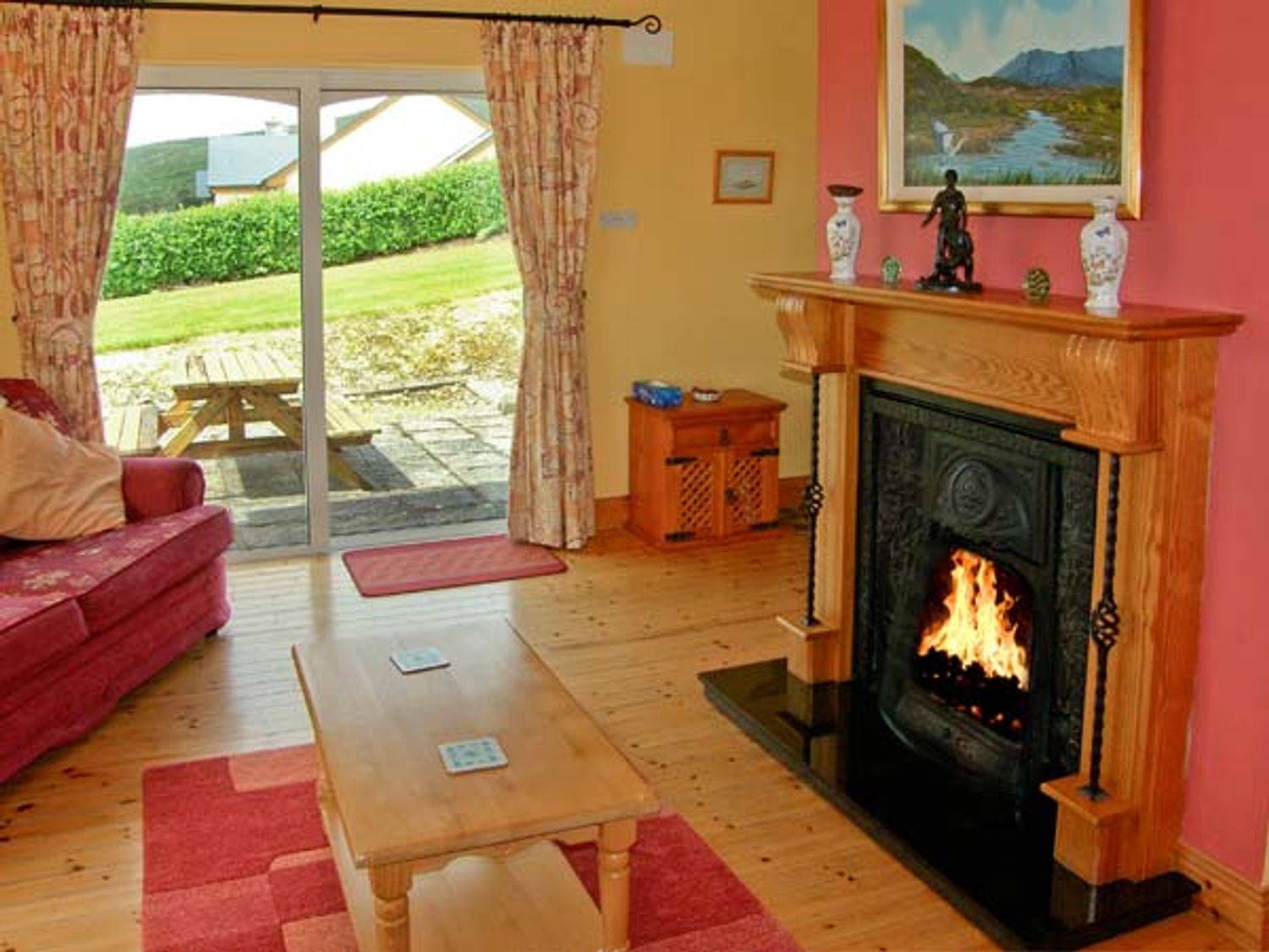 A living room with a fireplace a wooden coffee table a red sofa and a sliding glass door at Heron's Nest in Inch County Kerry