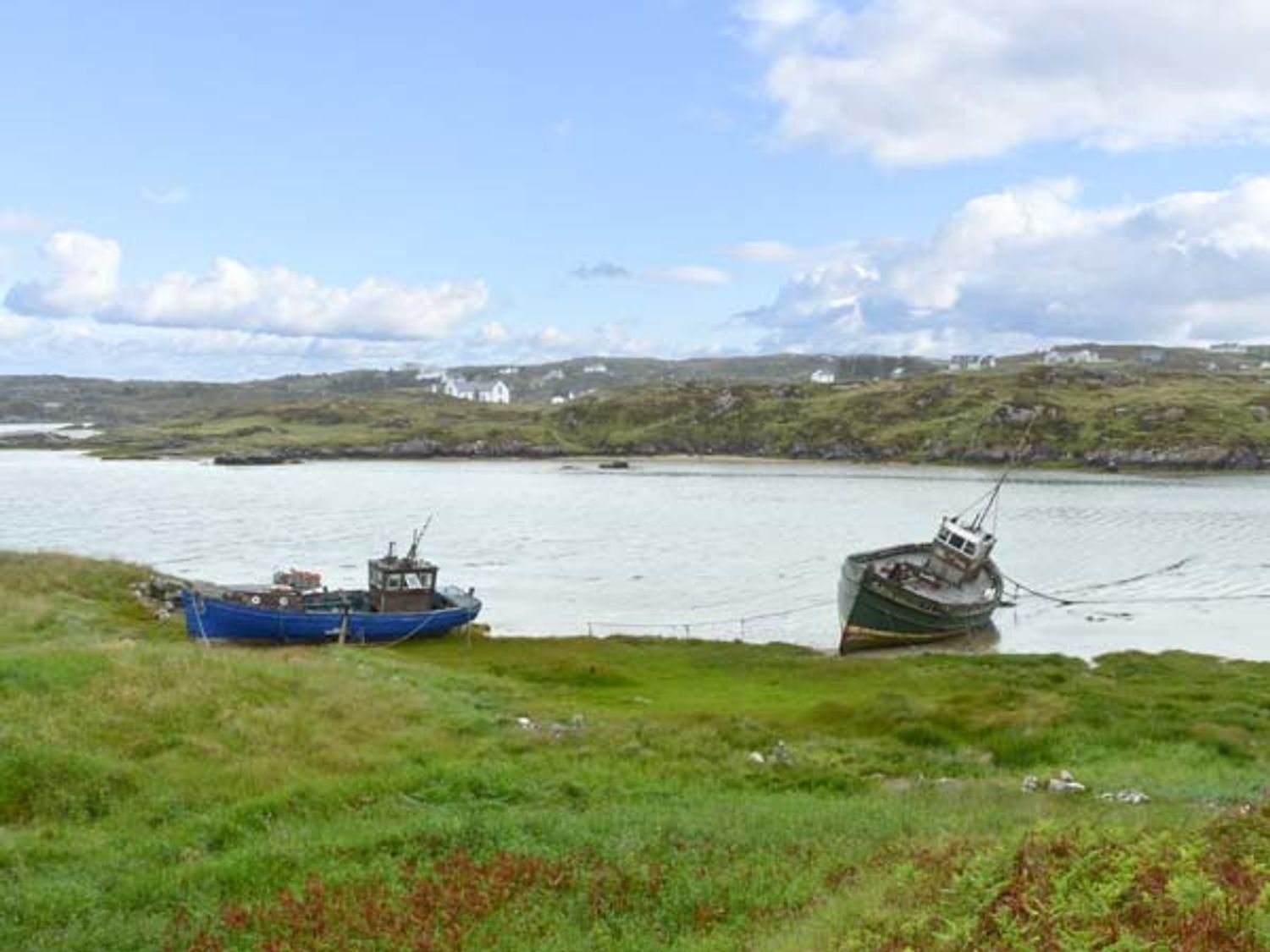 Two boats on the shore of a body of water with hills and houses in the background at Lully More Cottage in Cruit Island County Donegal