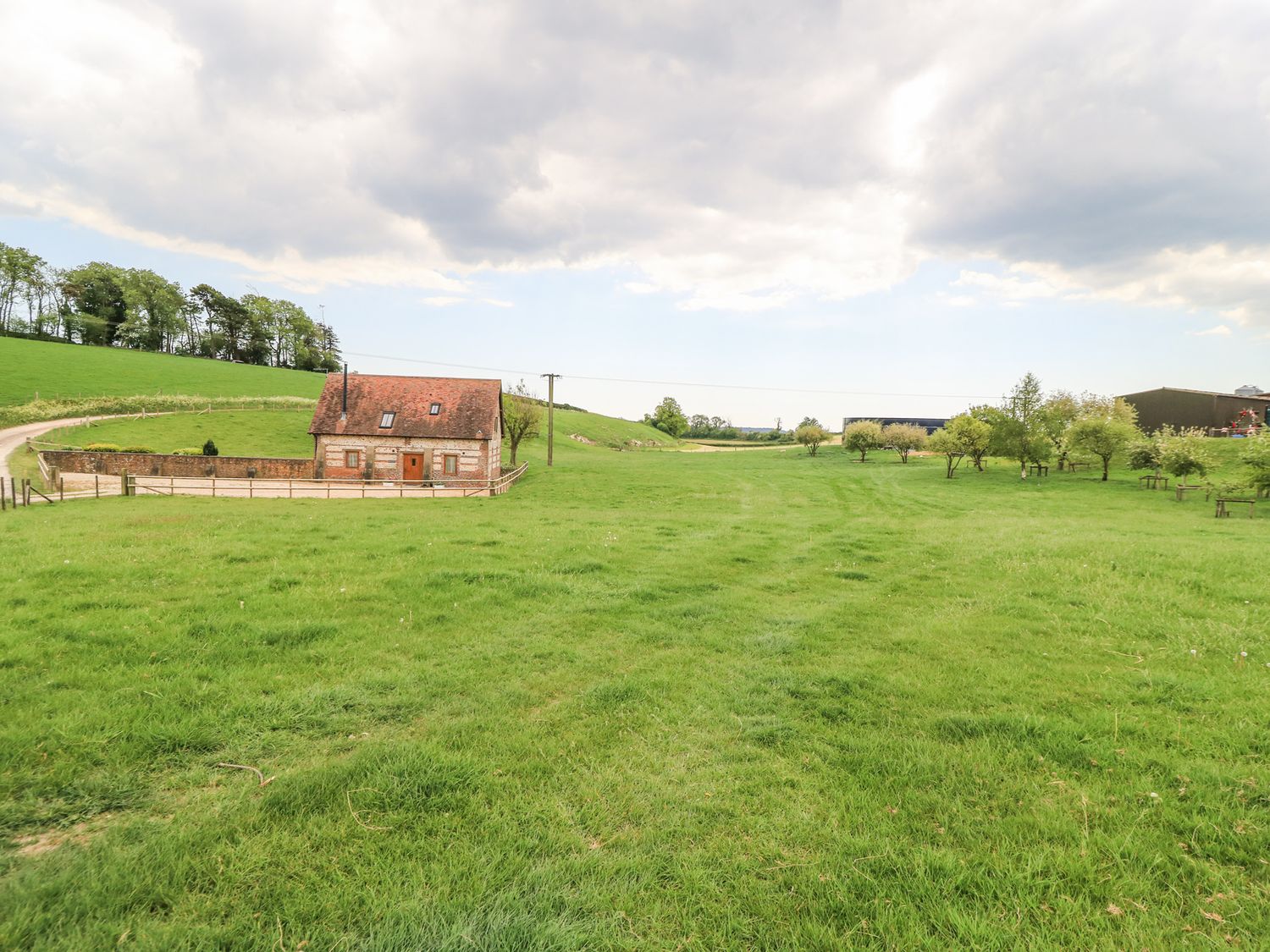 A small brick house with a red roof surrounded by a fenced green field and trees at Shepherd's Barn Between Milborne St Andrew and Winterborne Whitechurch