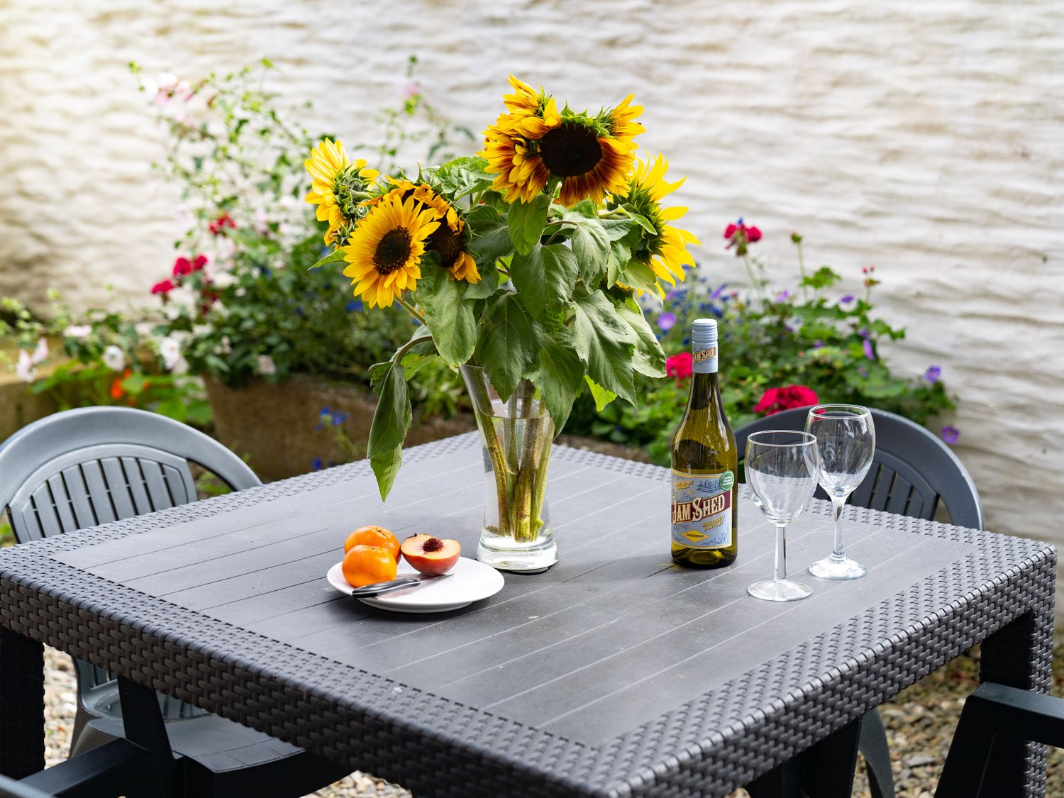 A table with a vase of sunflowers a bottle of wine two wine glasses and a plate of fruit on a patio at Y Cartws in Newport